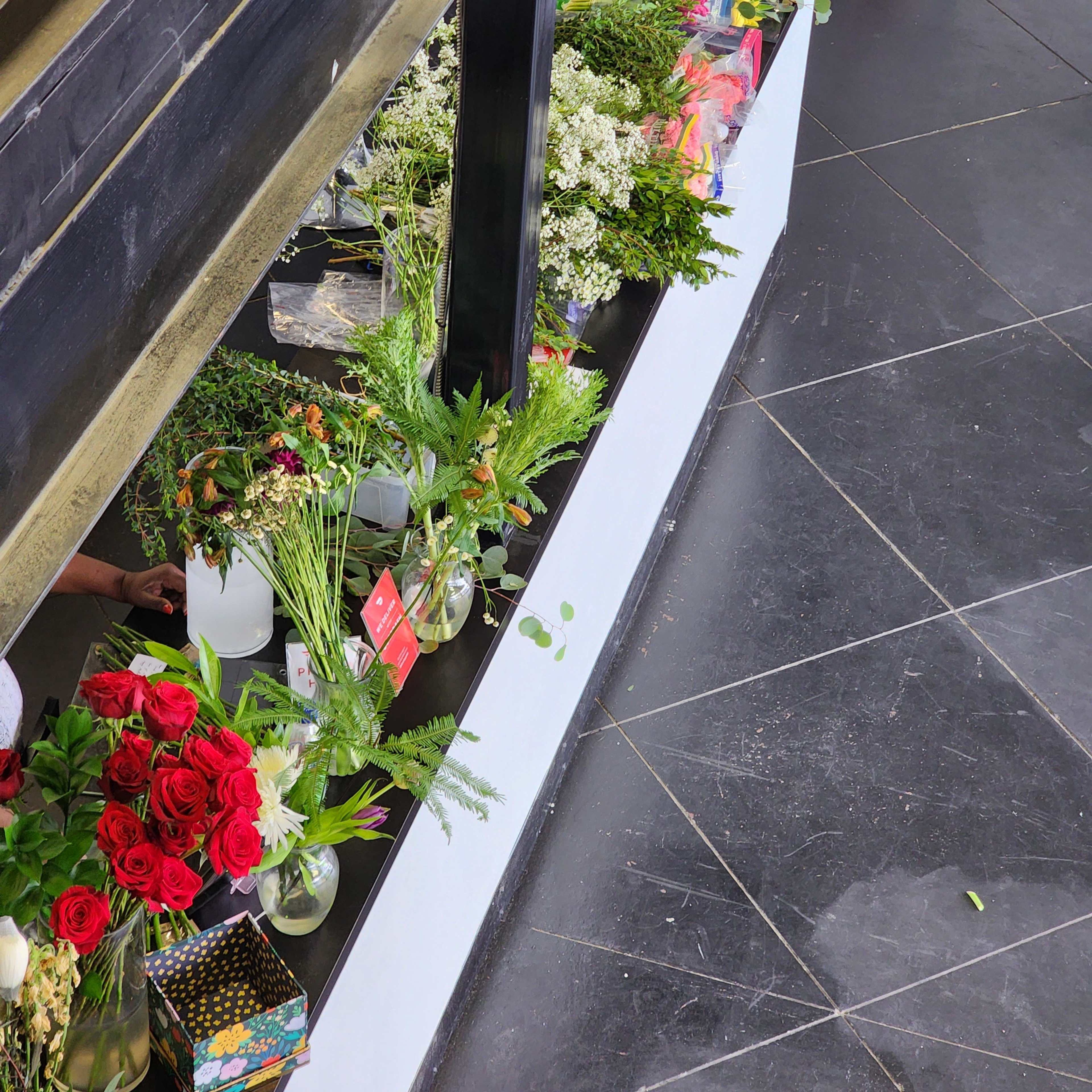 A display of various flowers and greenery is arranged on a counter in a shop with a dark tiled floor.