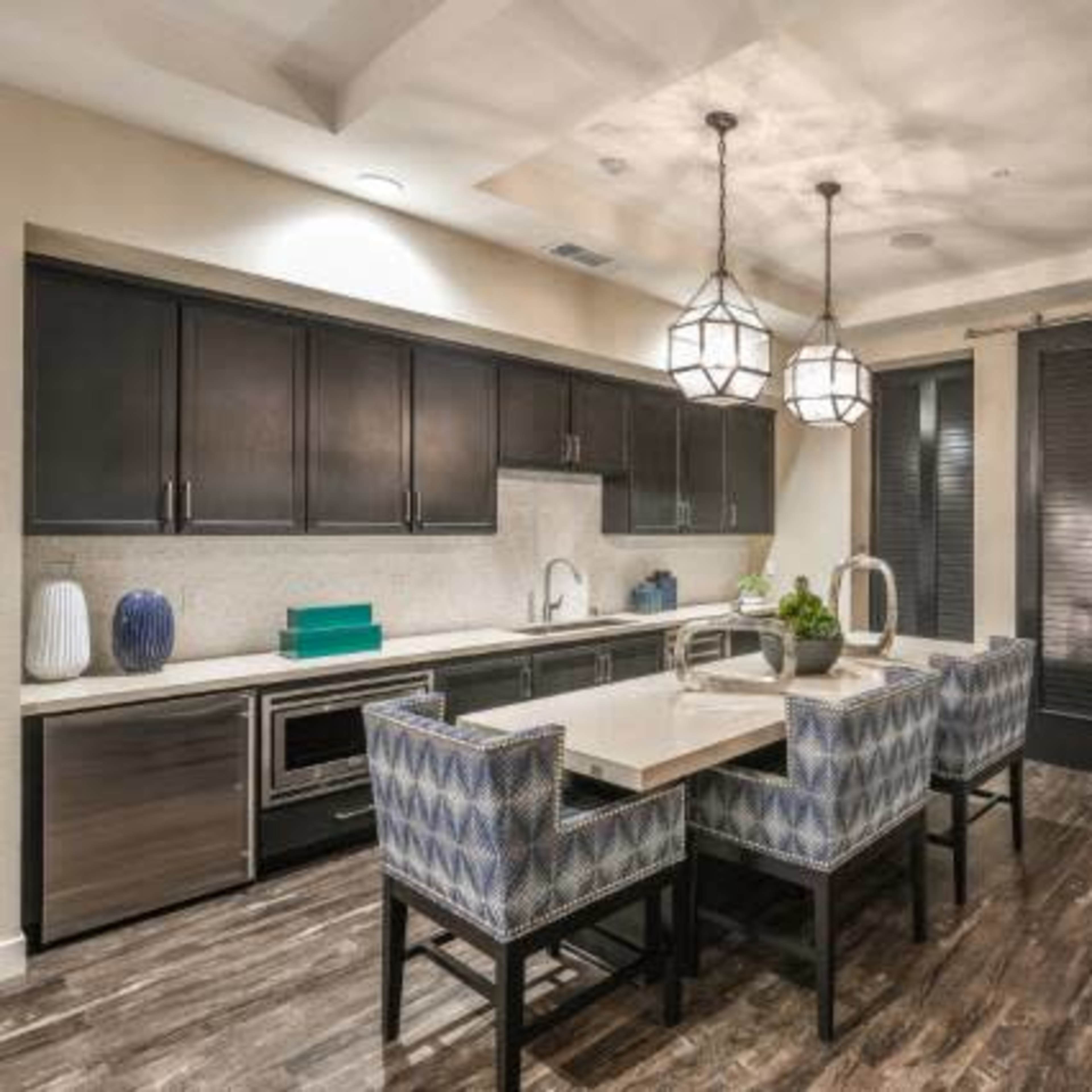 A modern kitchen and dining area with a table surrounded by patterned chairs, sleek cabinetry, and decorative pendant lights.