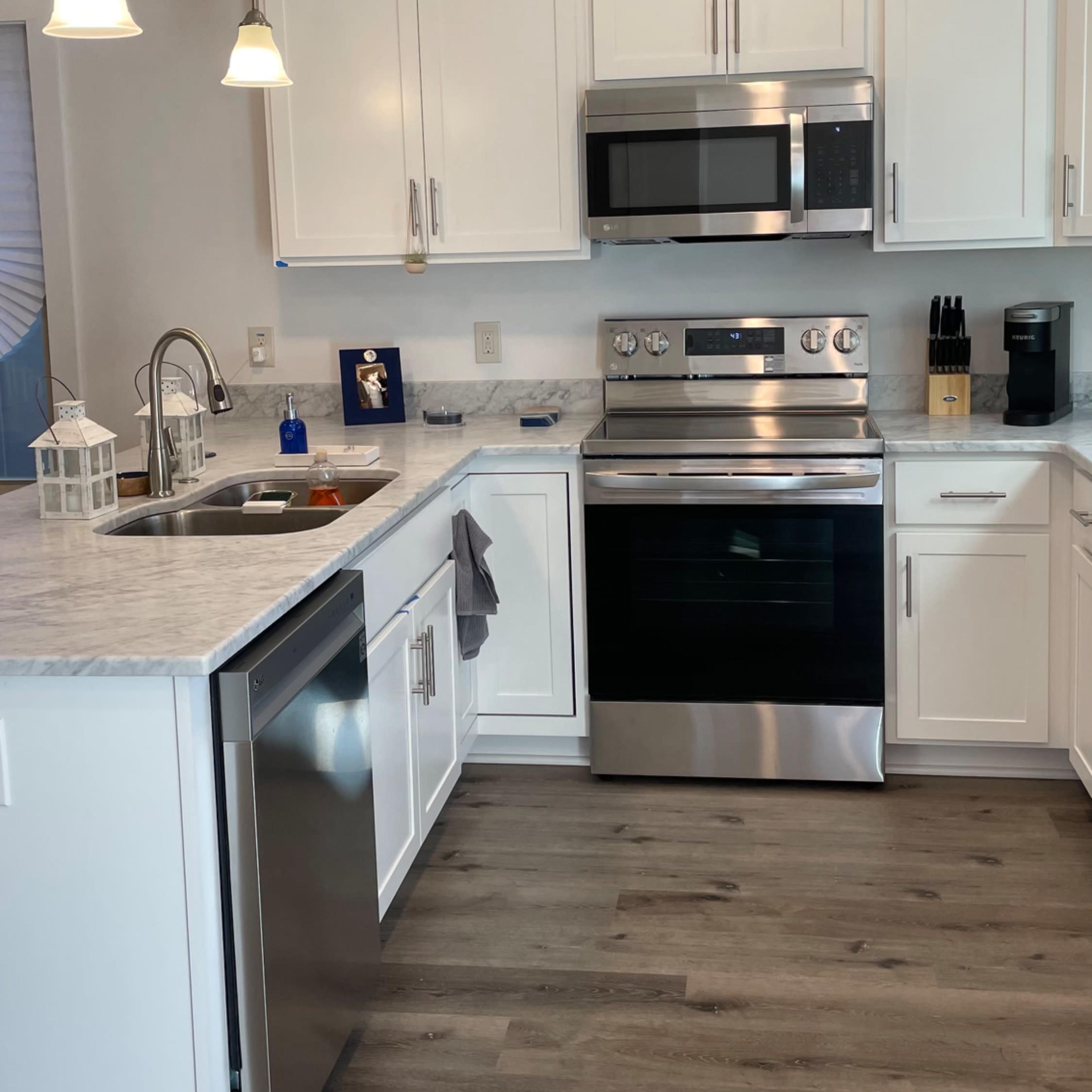 A modern kitchen featuring white cabinets, stainless steel appliances, and a marble countertop.