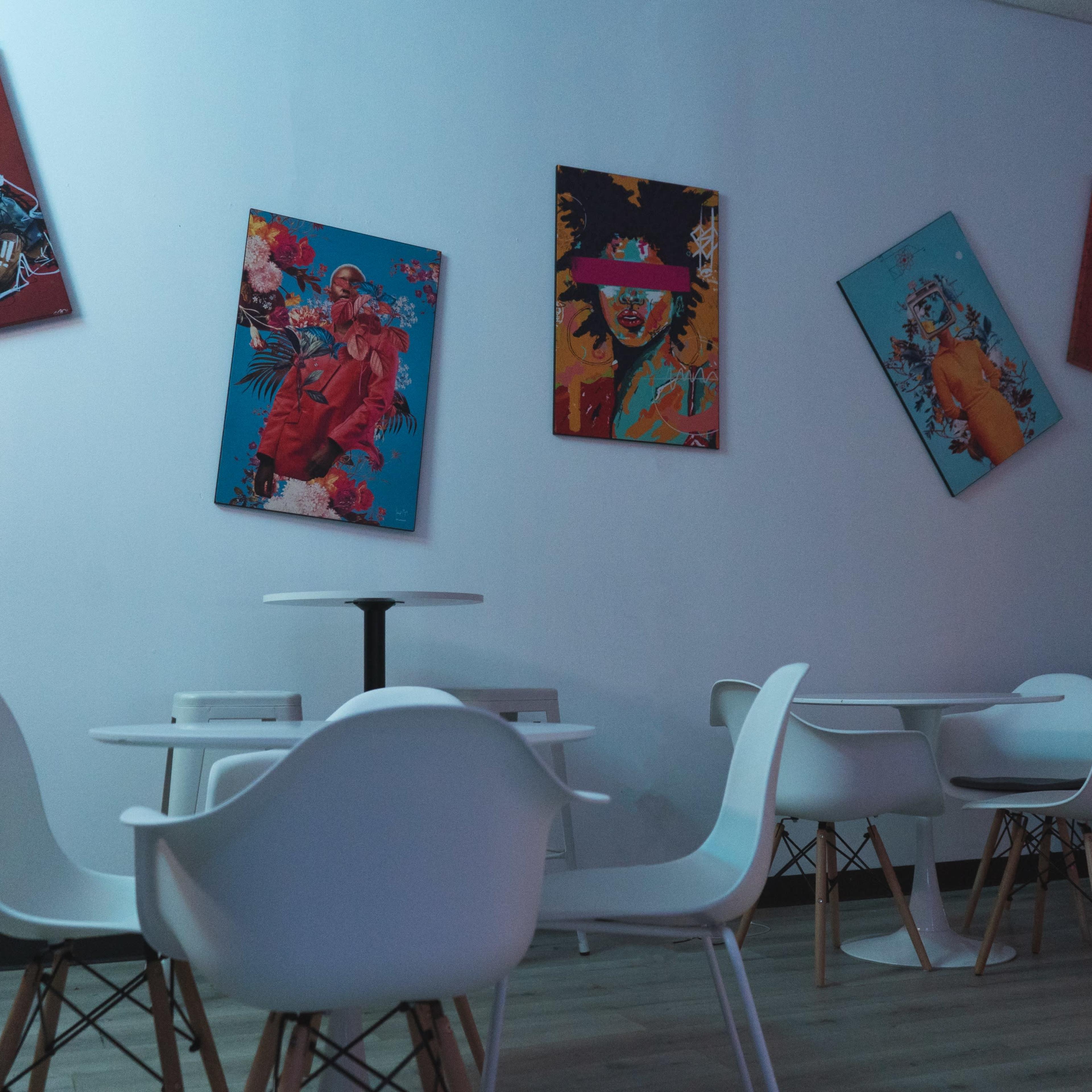 A modern indoor space featuring white chairs and tables arranged around a wall decorated with colorful artwork.