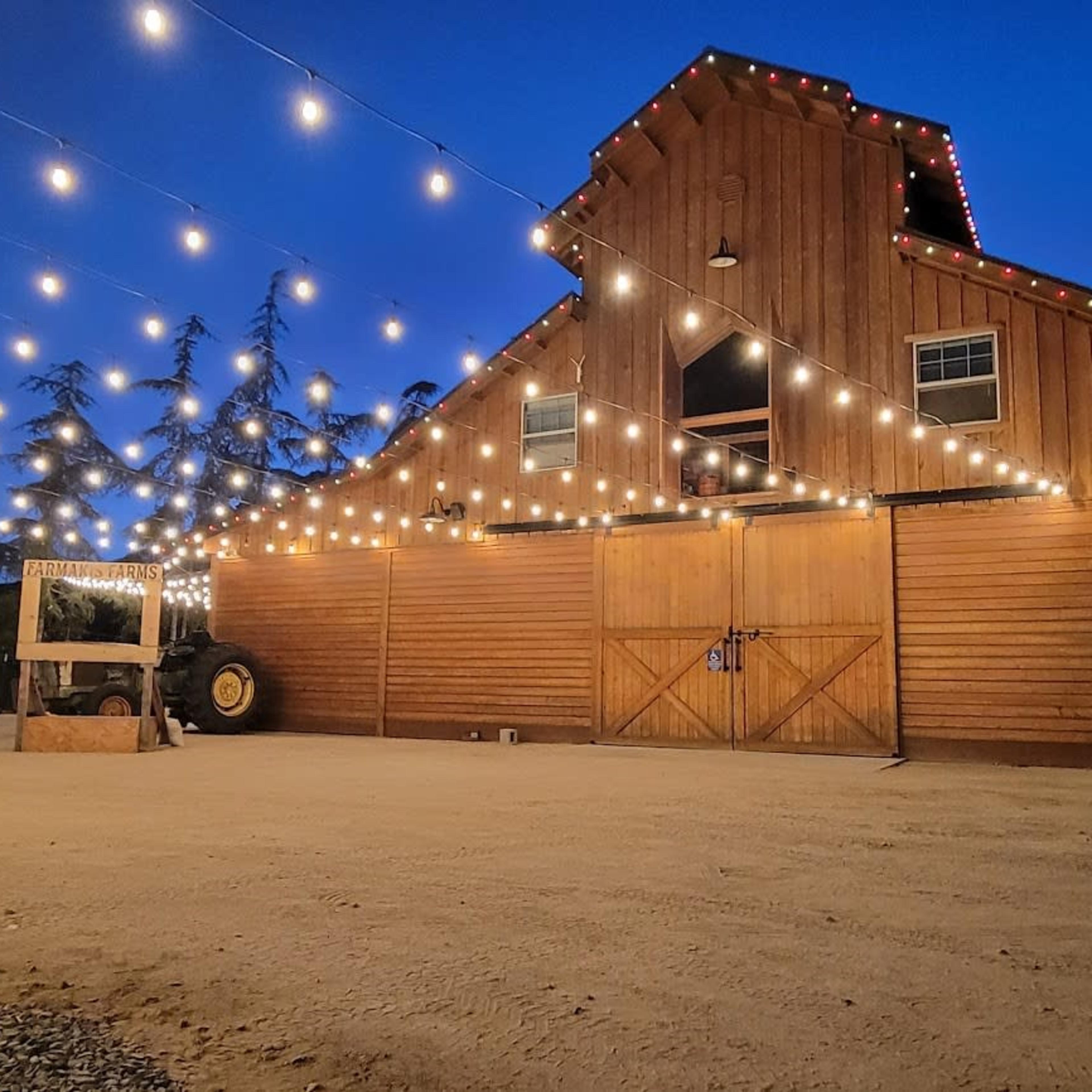 A wooden barn is illuminated by string lights against a twilight sky.