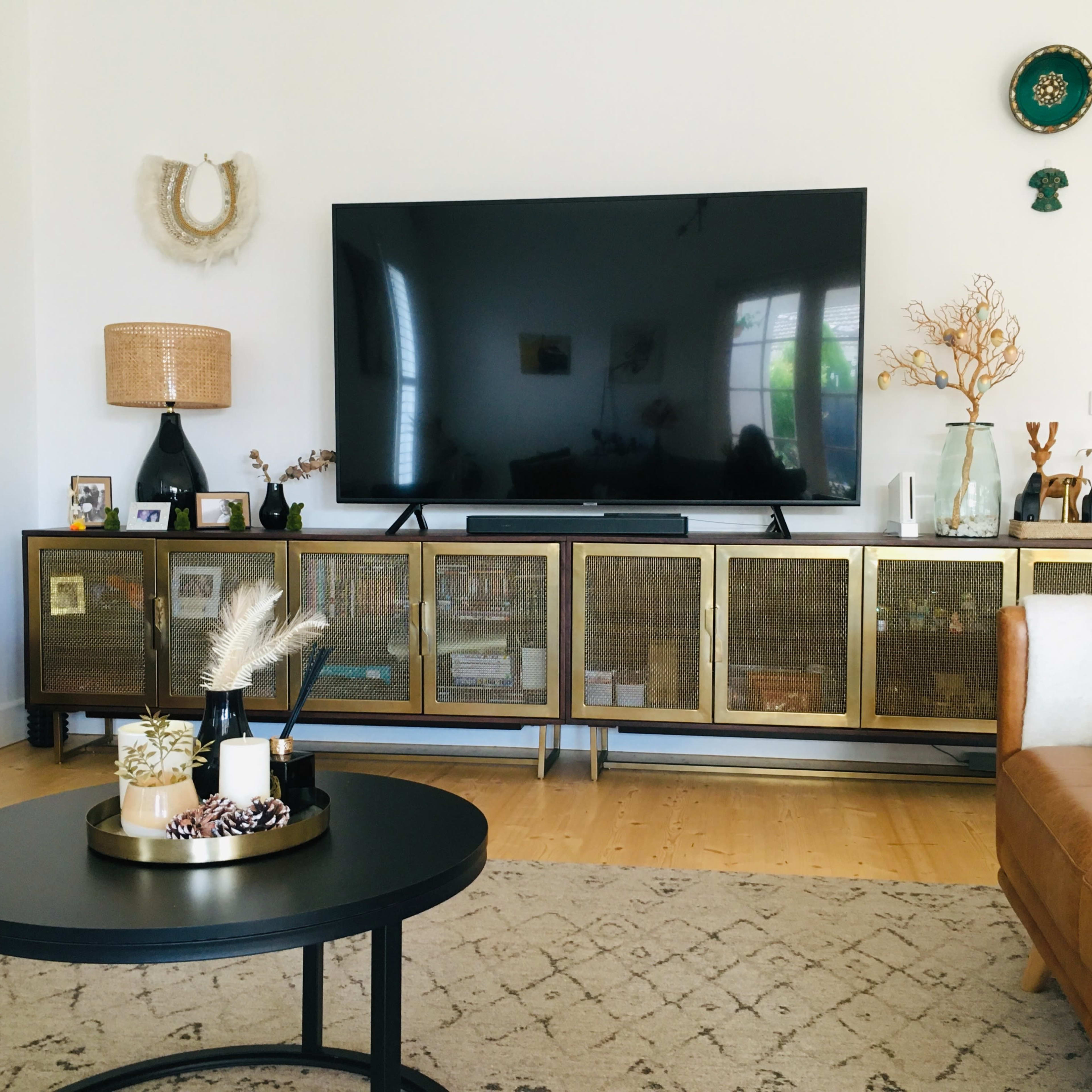 A modern living room featuring a large television mounted on the wall above a stylish media console with glass-paneled doors, surrounded by decorative items and plants.