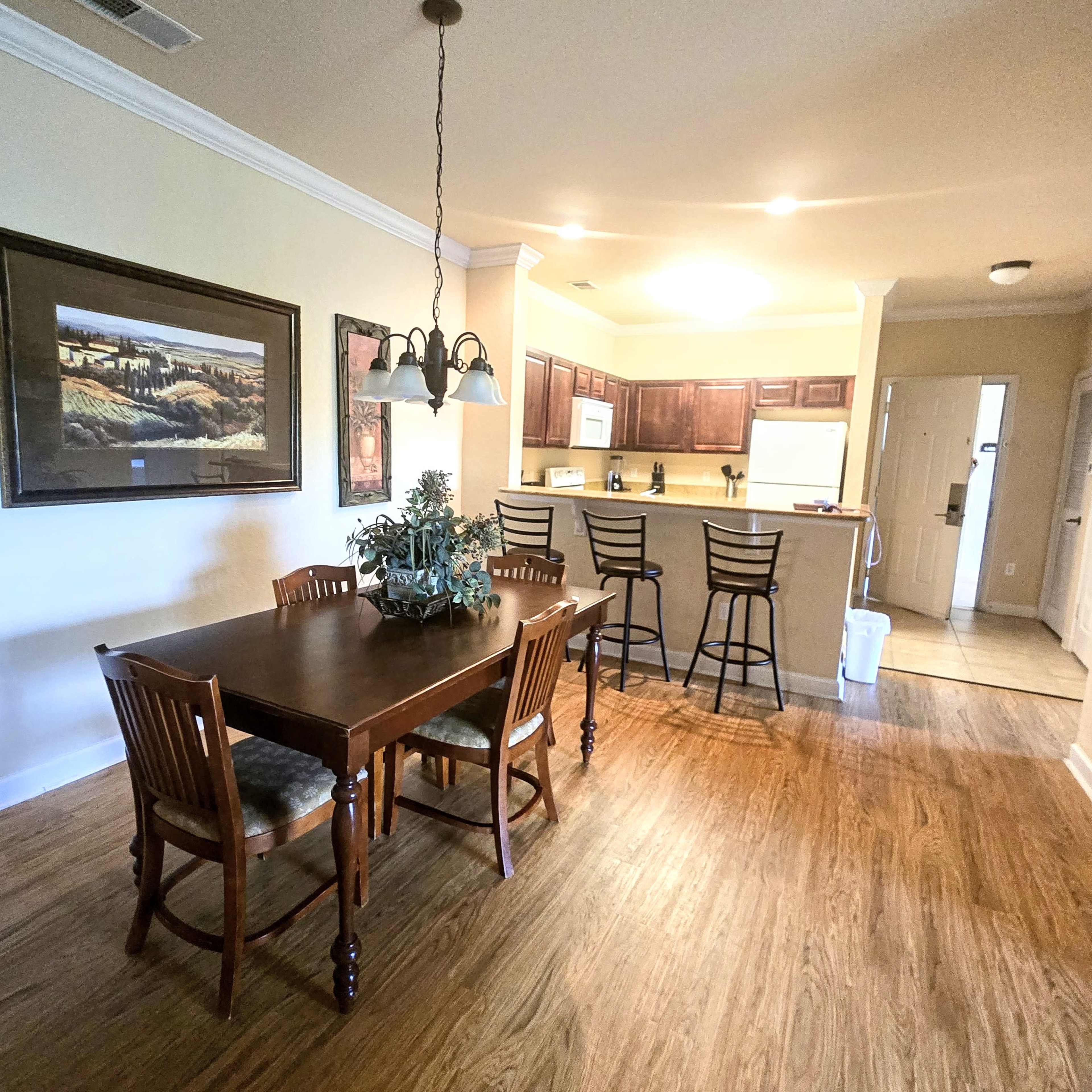 A dining area with a wooden table and chairs, leading into a kitchen with bar seating and dark cabinetry.