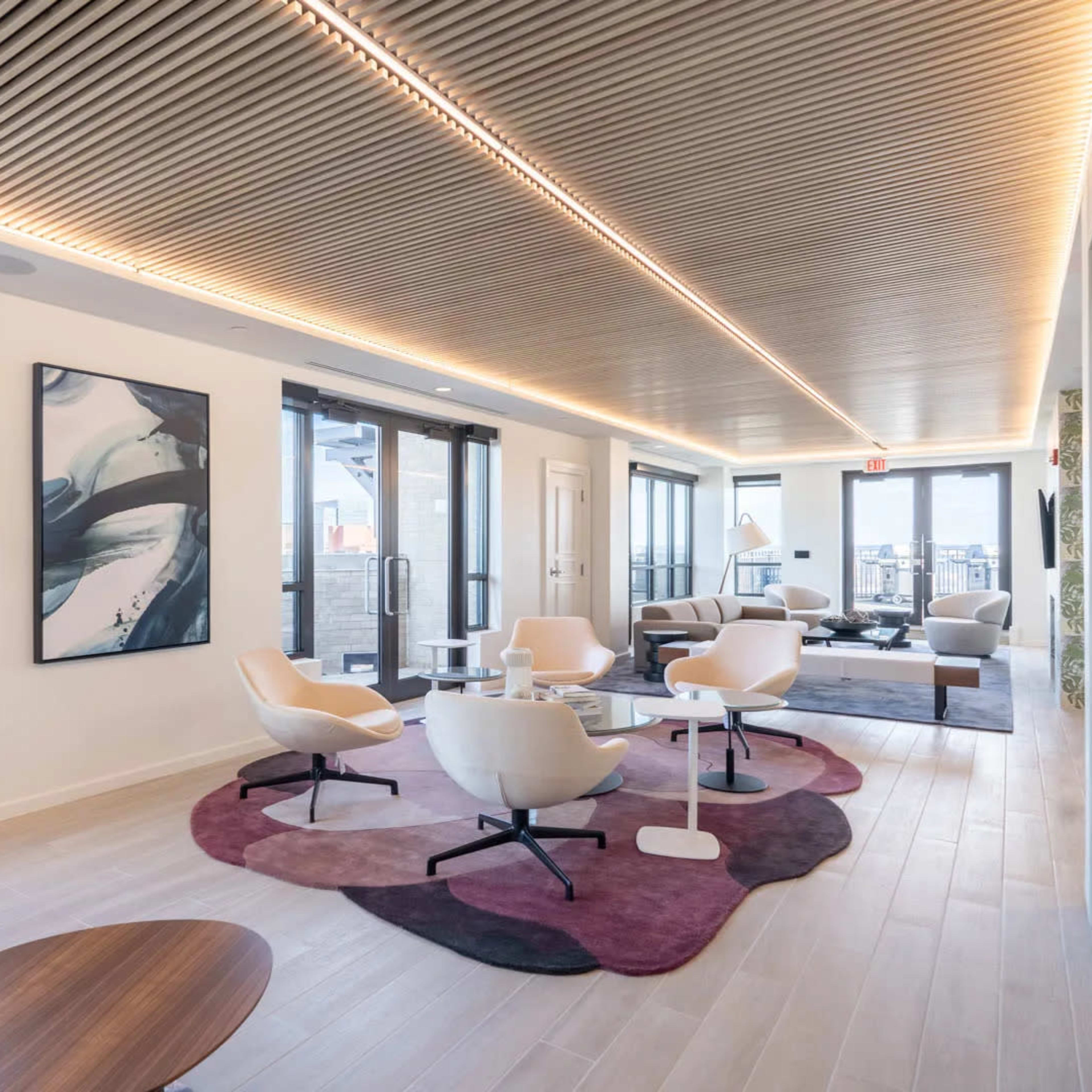 A modern lounge area with large windows, contemporary furniture, and a wooden ceiling.