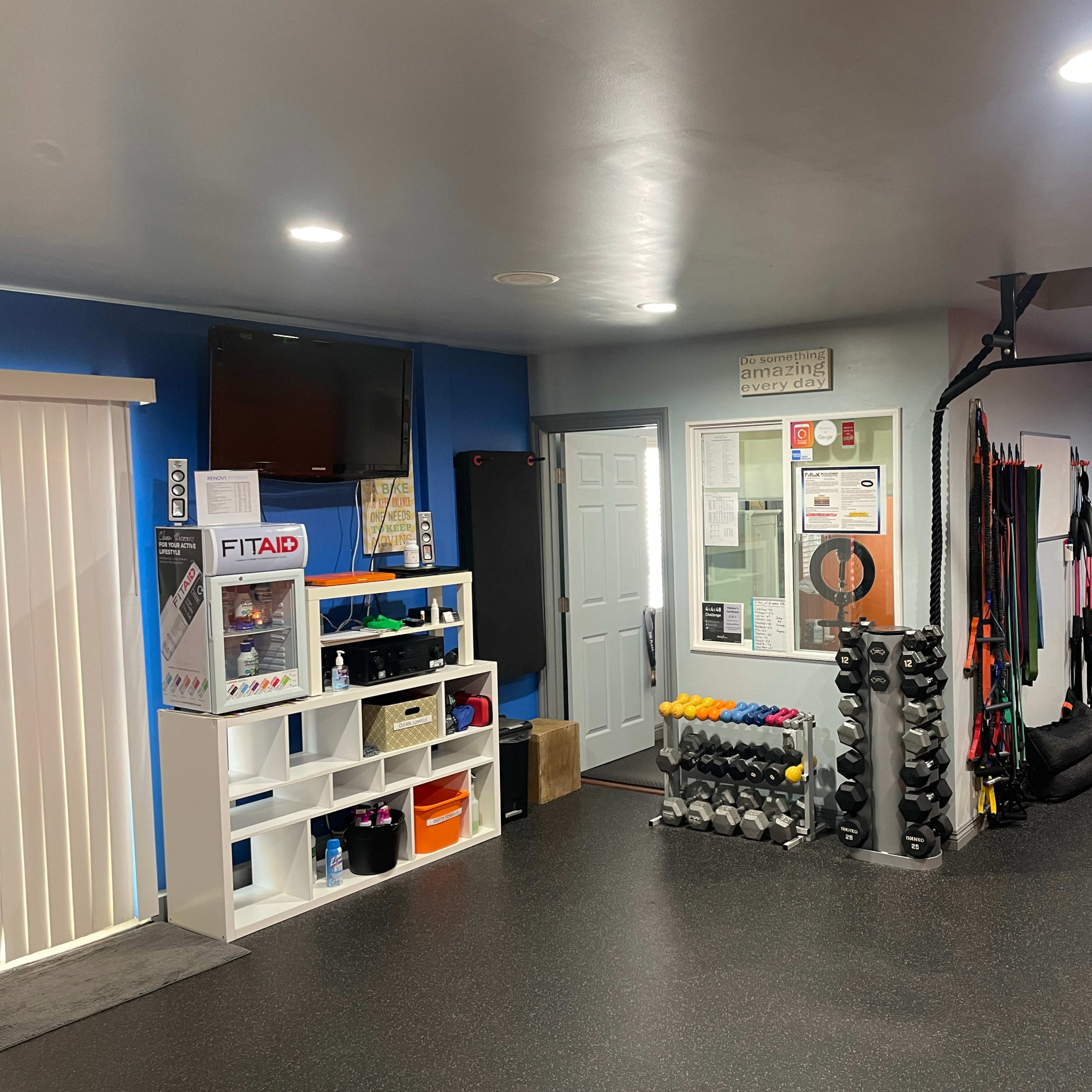A well-organized home gym featuring a variety of fitness equipment, a shelving unit with storage bins, and a wall-mounted television.