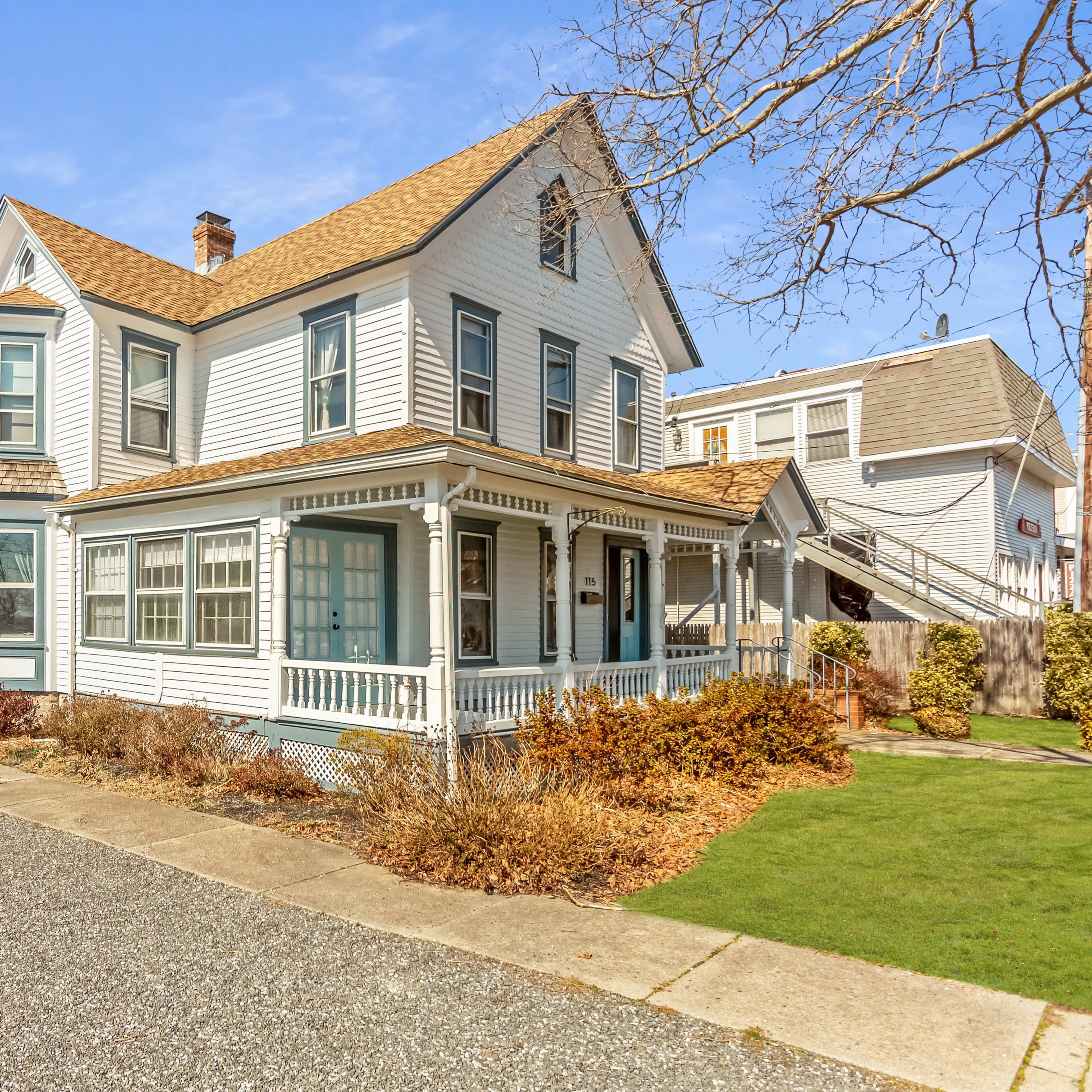 A large, two-story Victorian-style house with a wraparound porch and a gravel driveway, surrounded by landscaped yards.