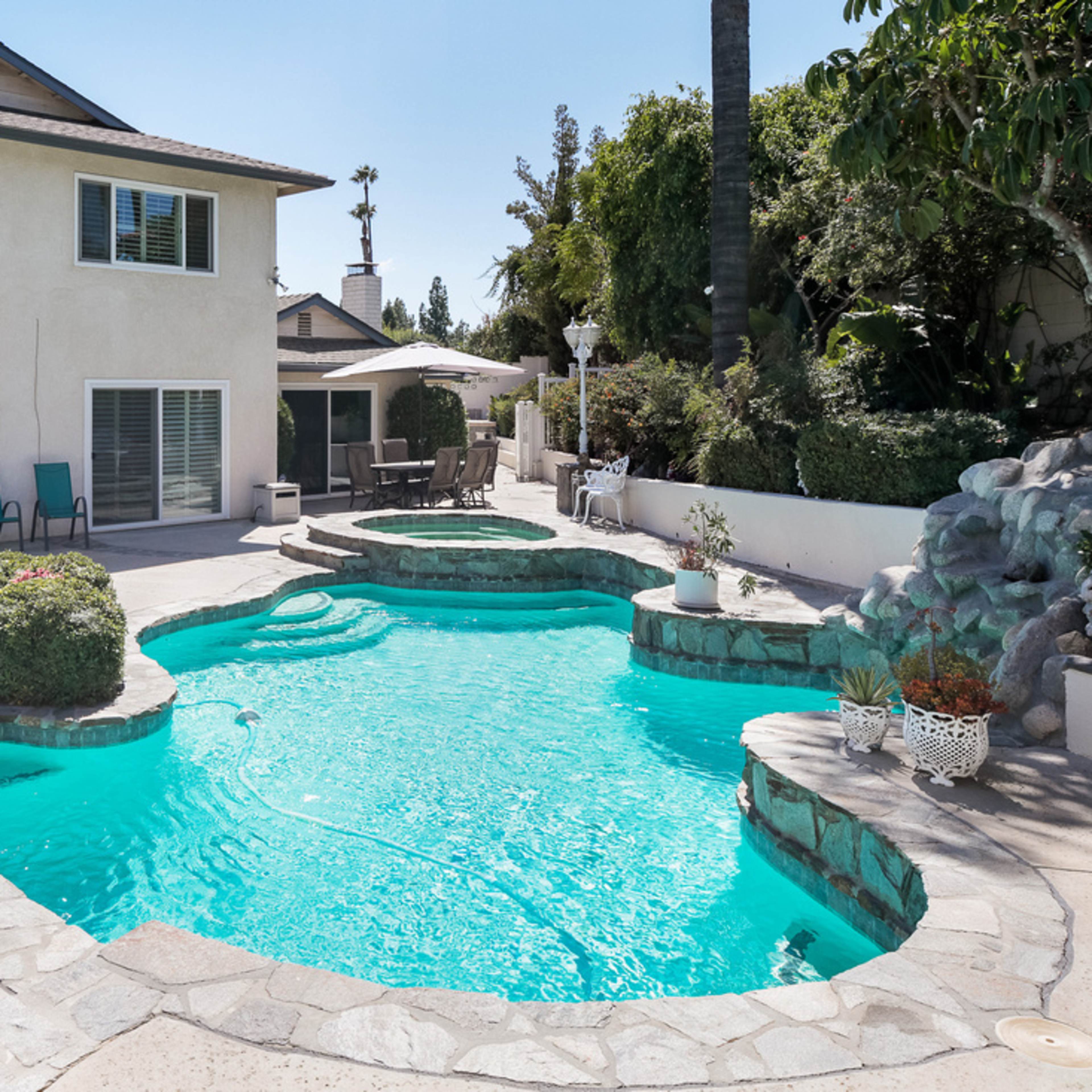 A backyard with a large swimming pool, a spa, and a two-story house in the background.
