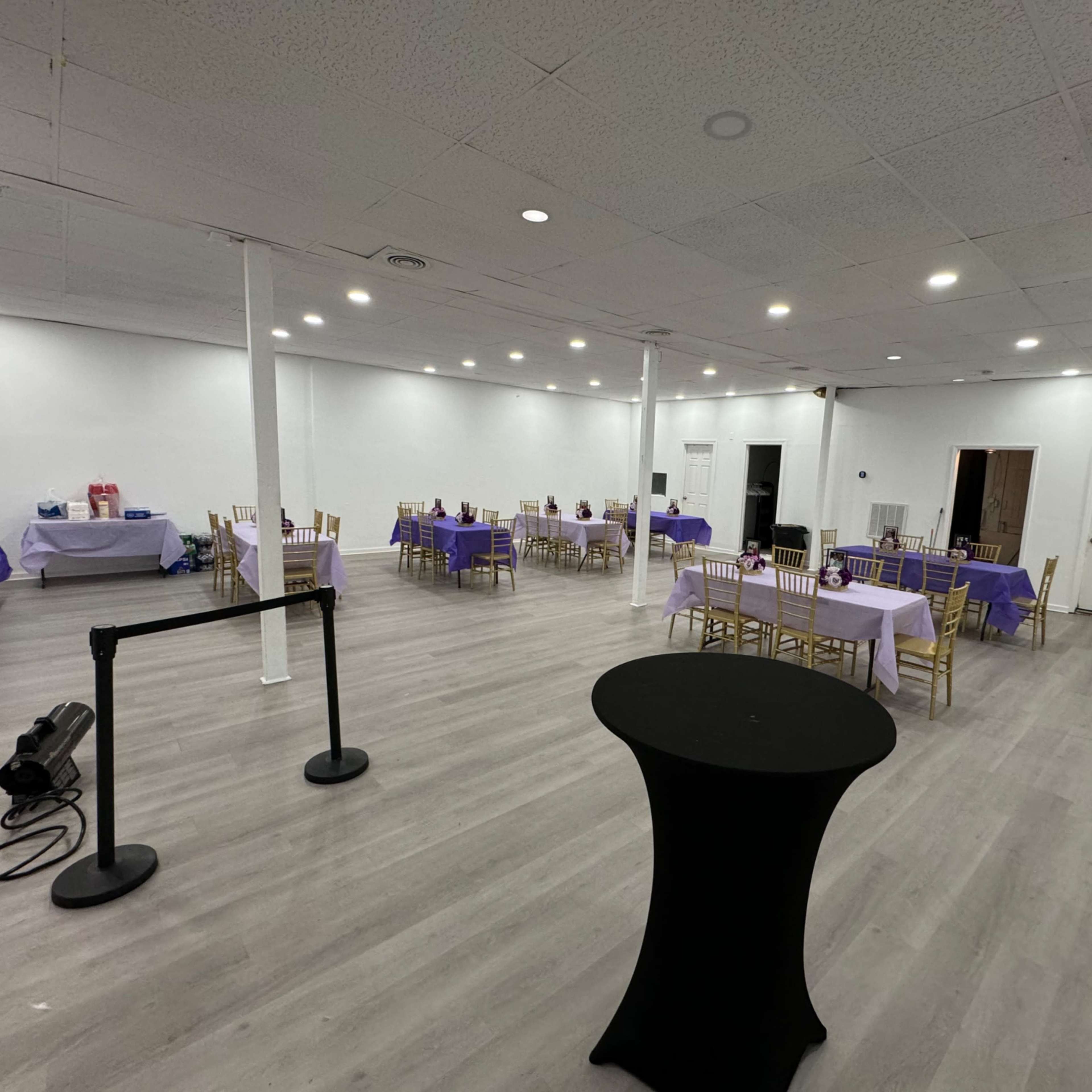A spacious, empty event room with several tables covered in purple tablecloths and arranged with gold chairs.