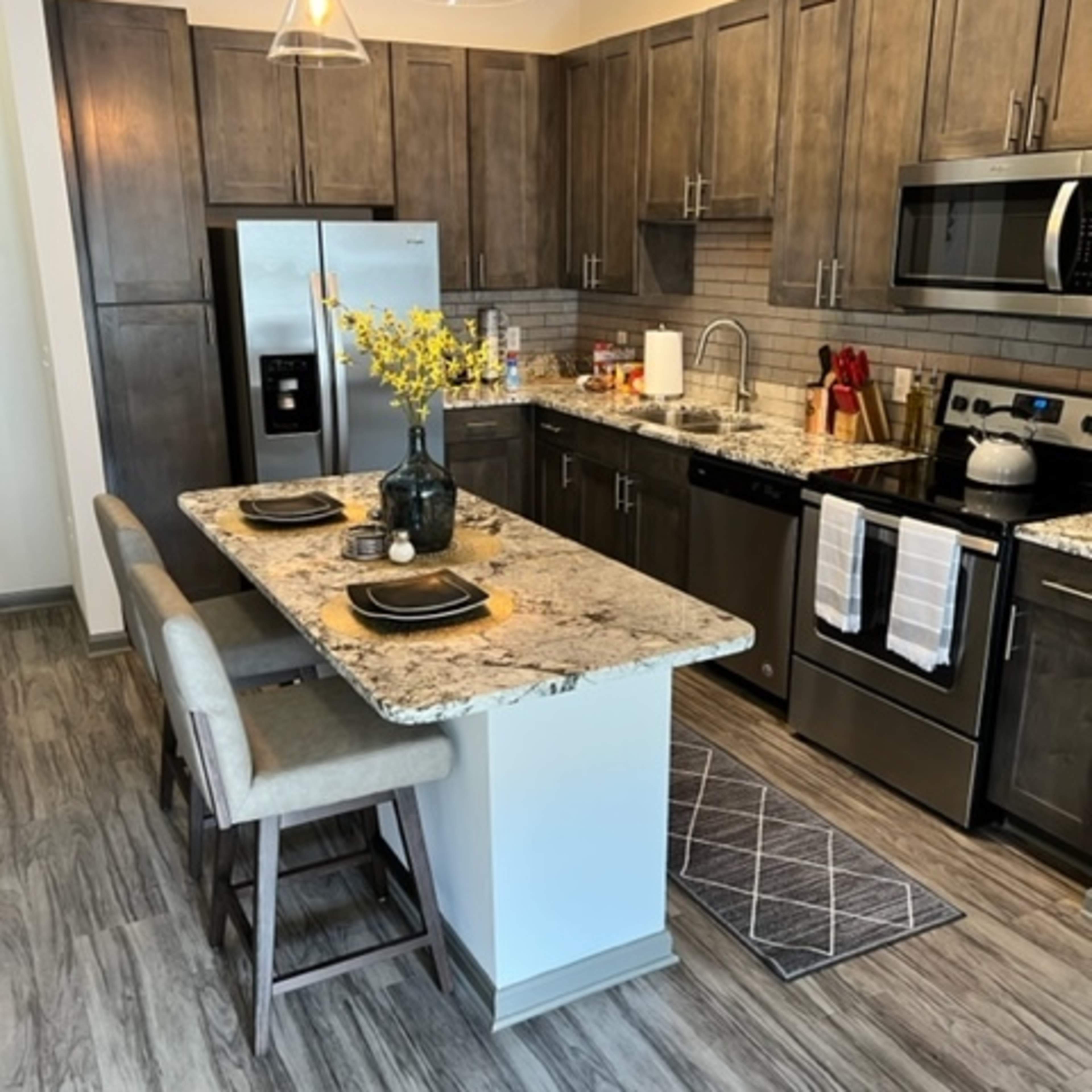 A modern kitchen with wooden cabinets, stainless steel appliances, a granite countertop, and a small island with seating.