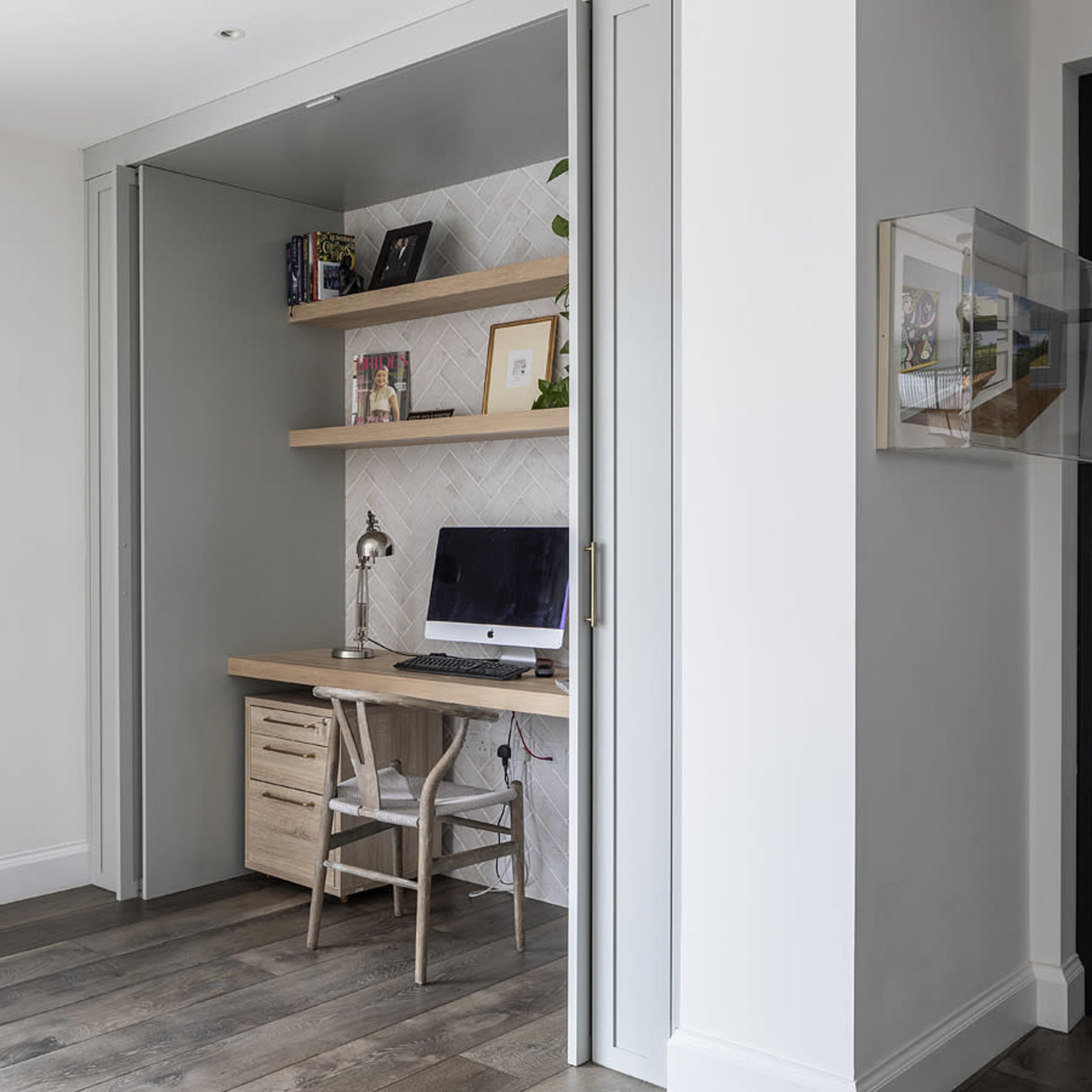 A small home office nook with a desk, a computer, and wooden shelving set against a light-colored wall.