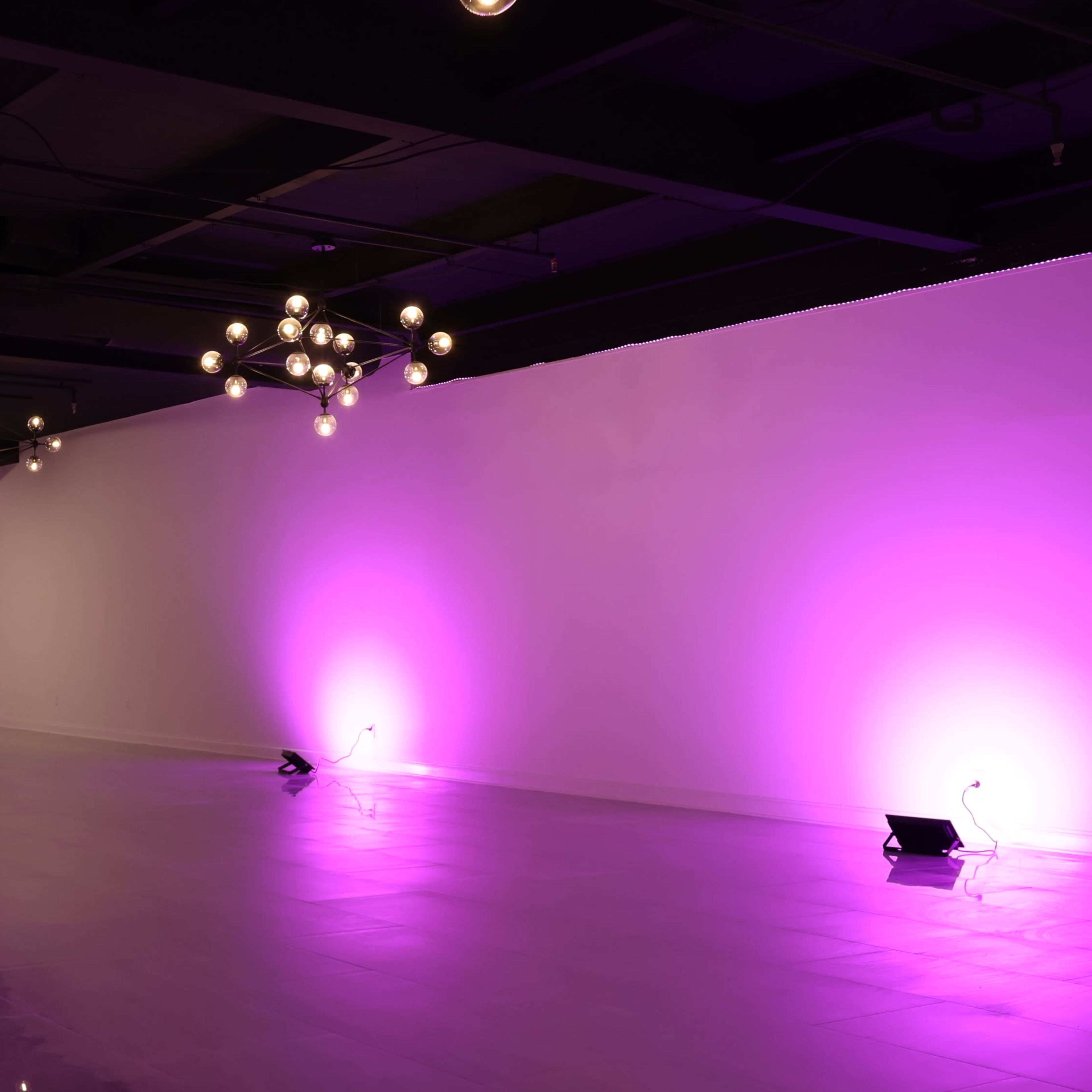 A spacious, empty room with modern lighting fixtures and purple ambient lighting on the walls.