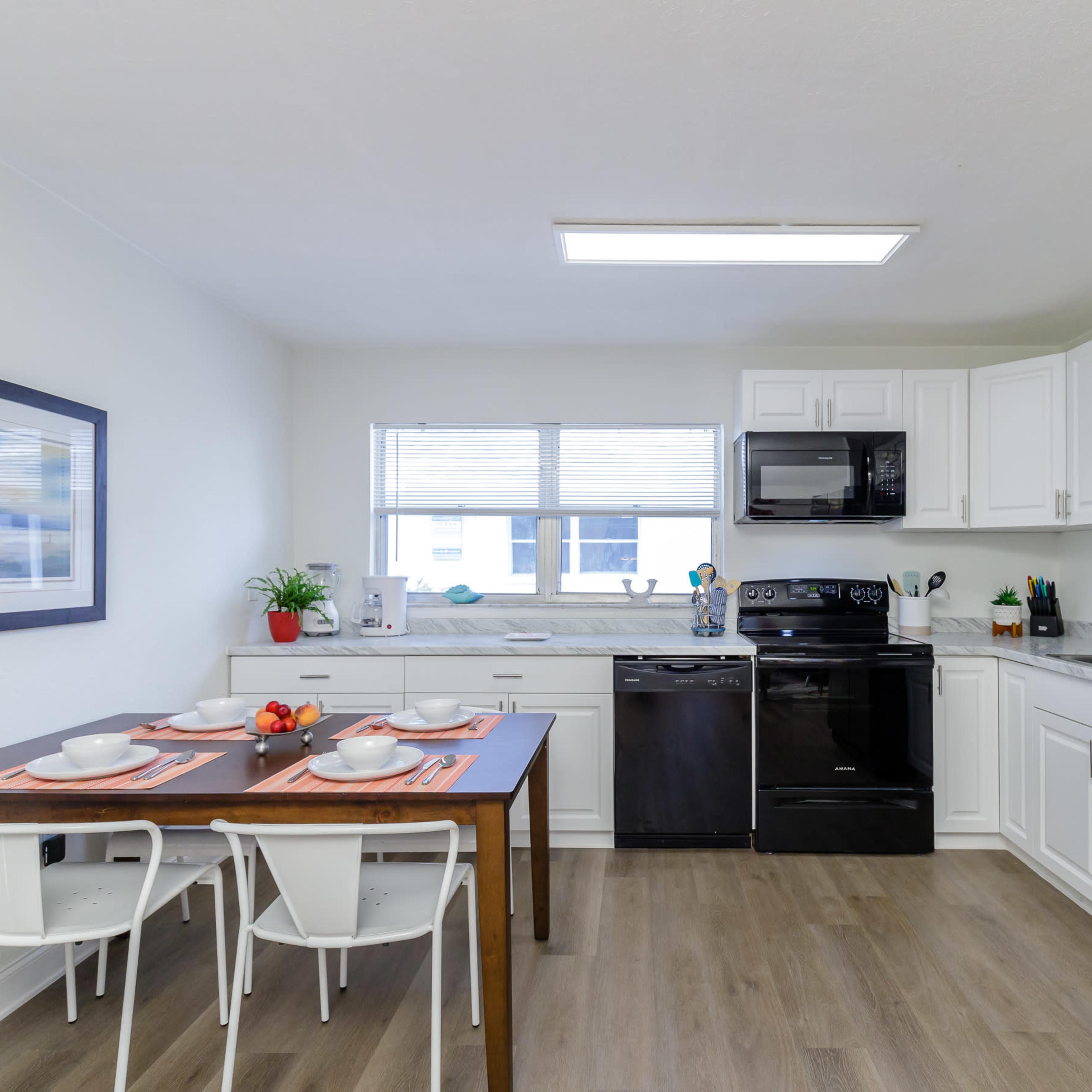 A modern kitchen features white cabinetry, black appliances, and a dining table set for two.