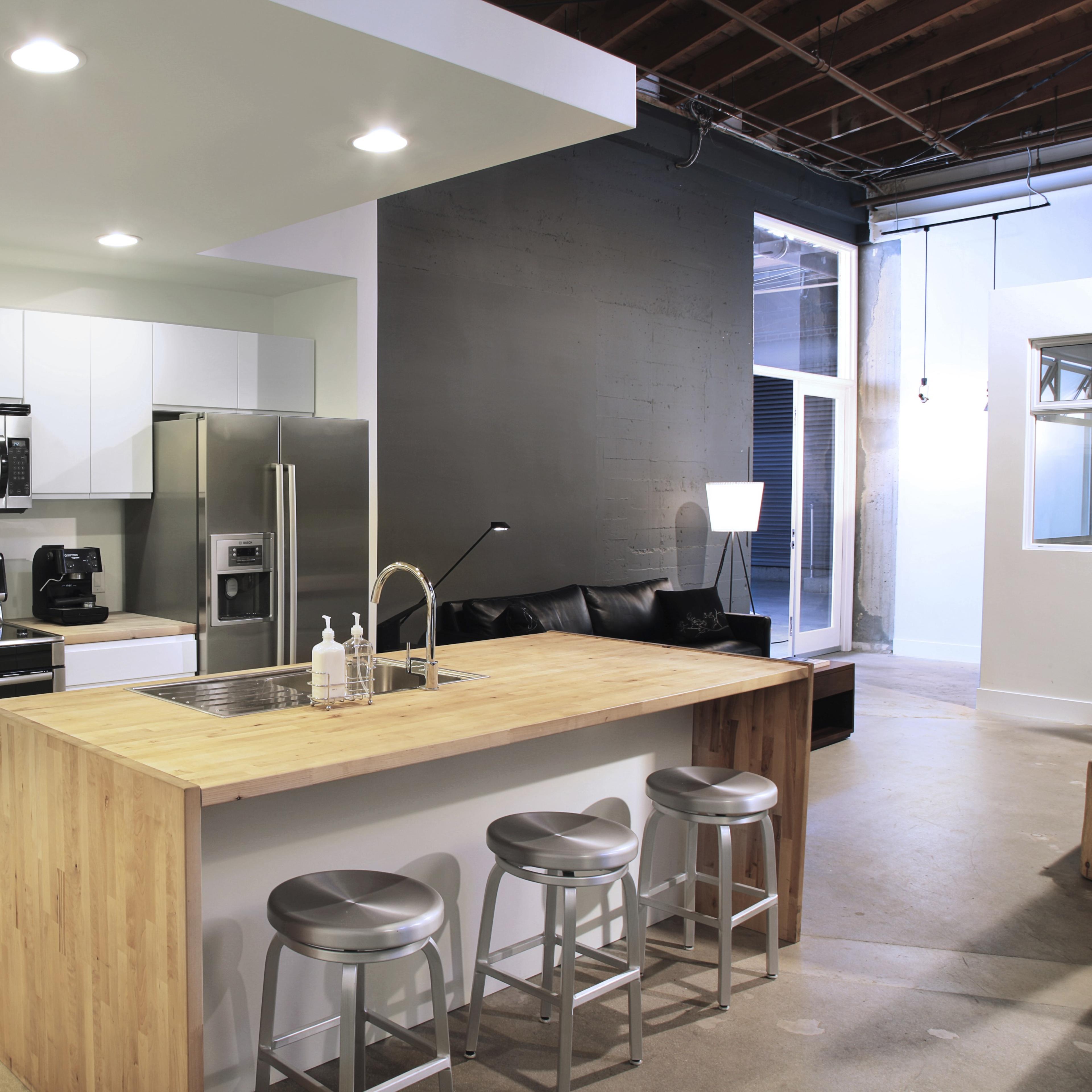 A modern kitchen with white cabinetry, stainless steel appliances, and a large wooden island with three metal stools.