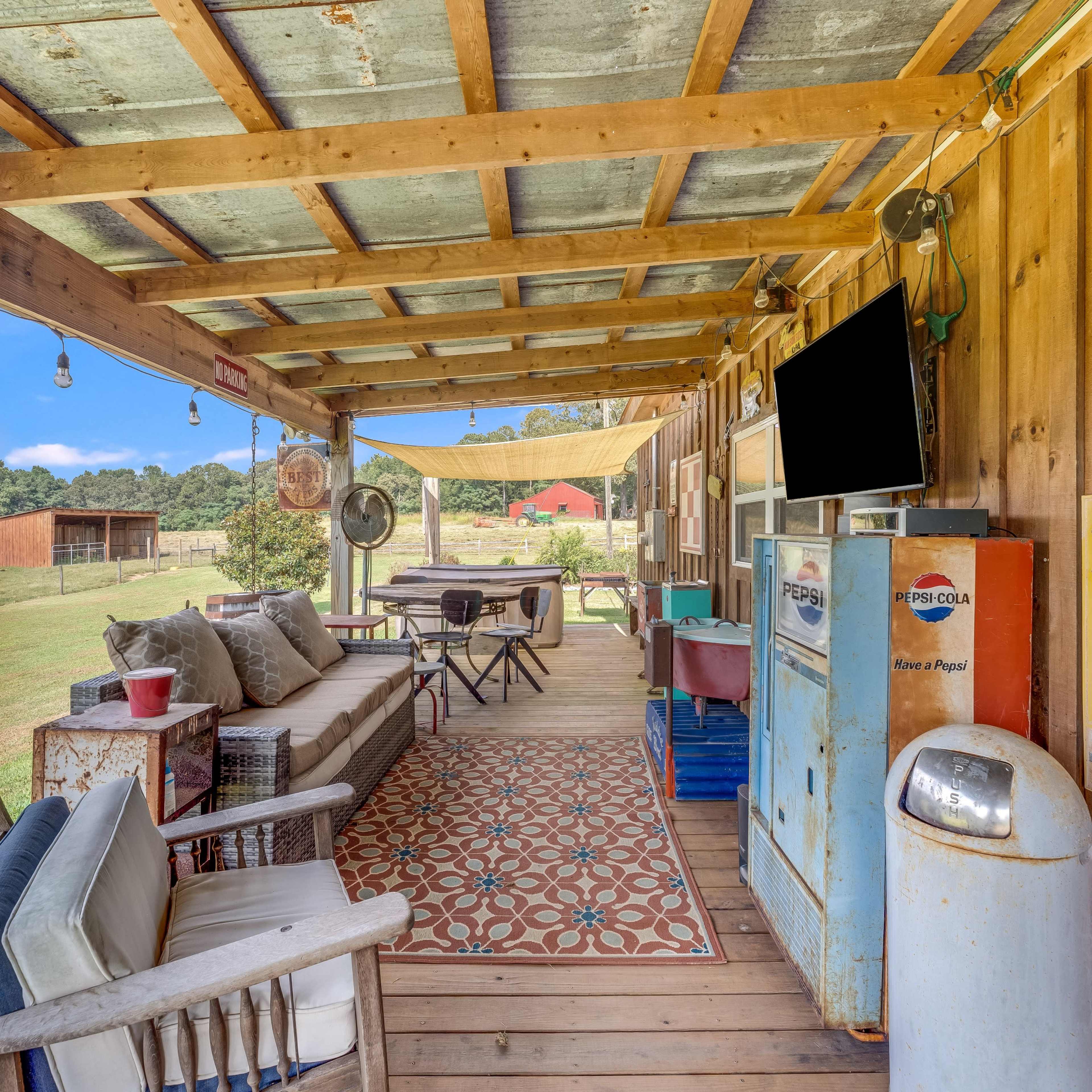 A rustic porch with seating, vintage advertising signage, and a view of a grassy field and barn in the background.