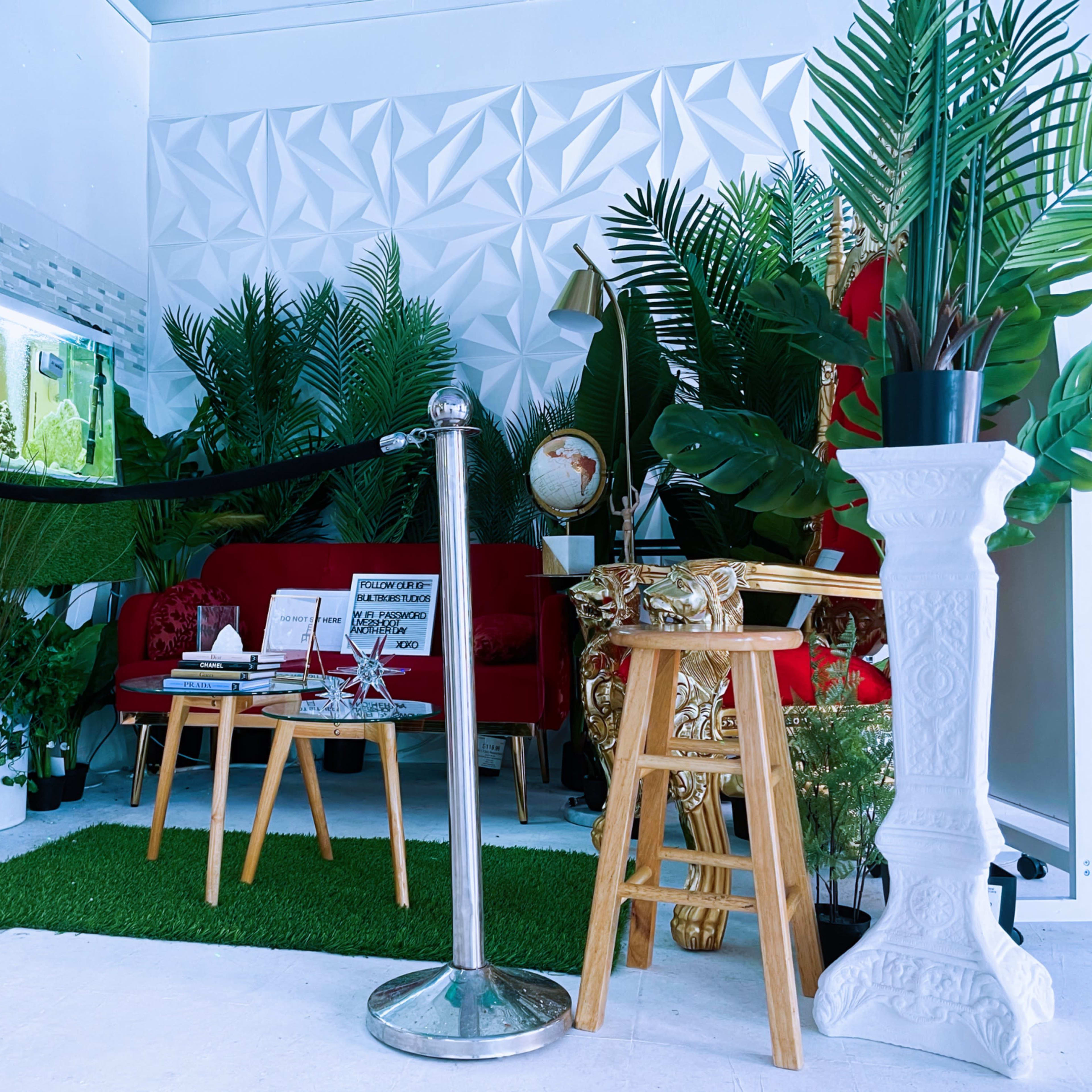 The scene features a modern indoor space filled with various potted plants, a red sofa, a small table, and an aquarium, creating a cozy, green atmosphere.
