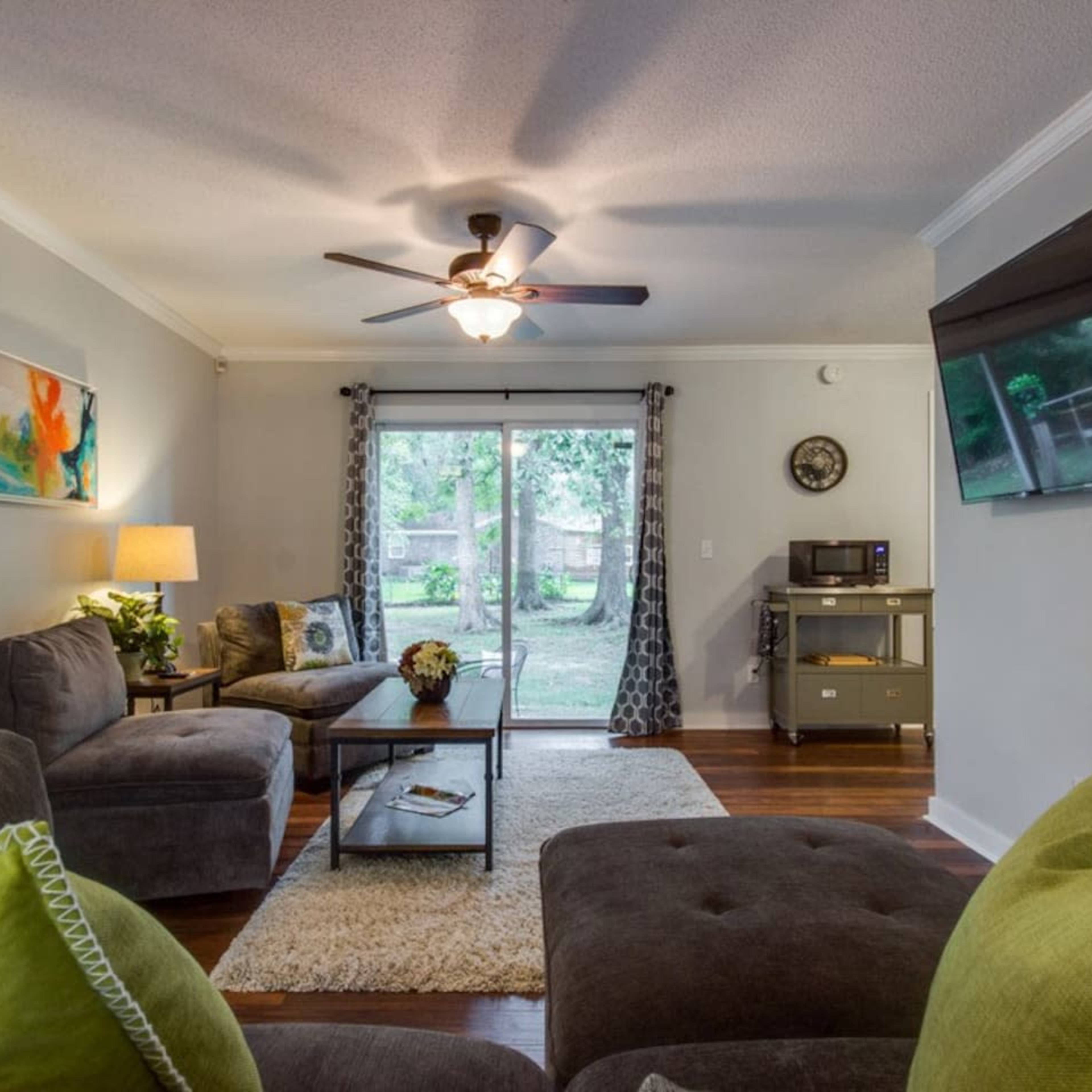 The living room features a sofa, armchair, and coffee table positioned around a large window that opens to a view of a backyard.