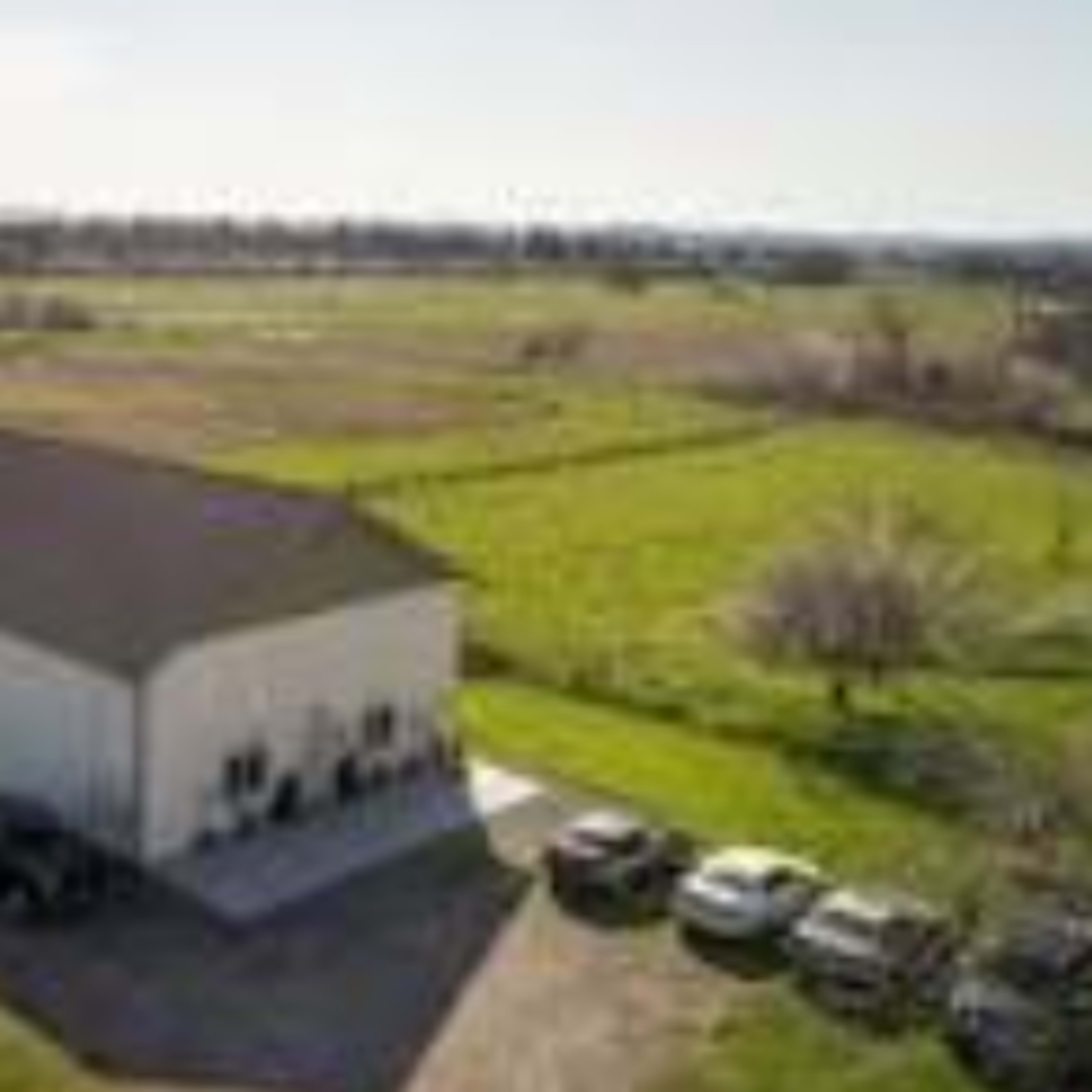 A large white building surrounded by green fields and several parked vehicles.
