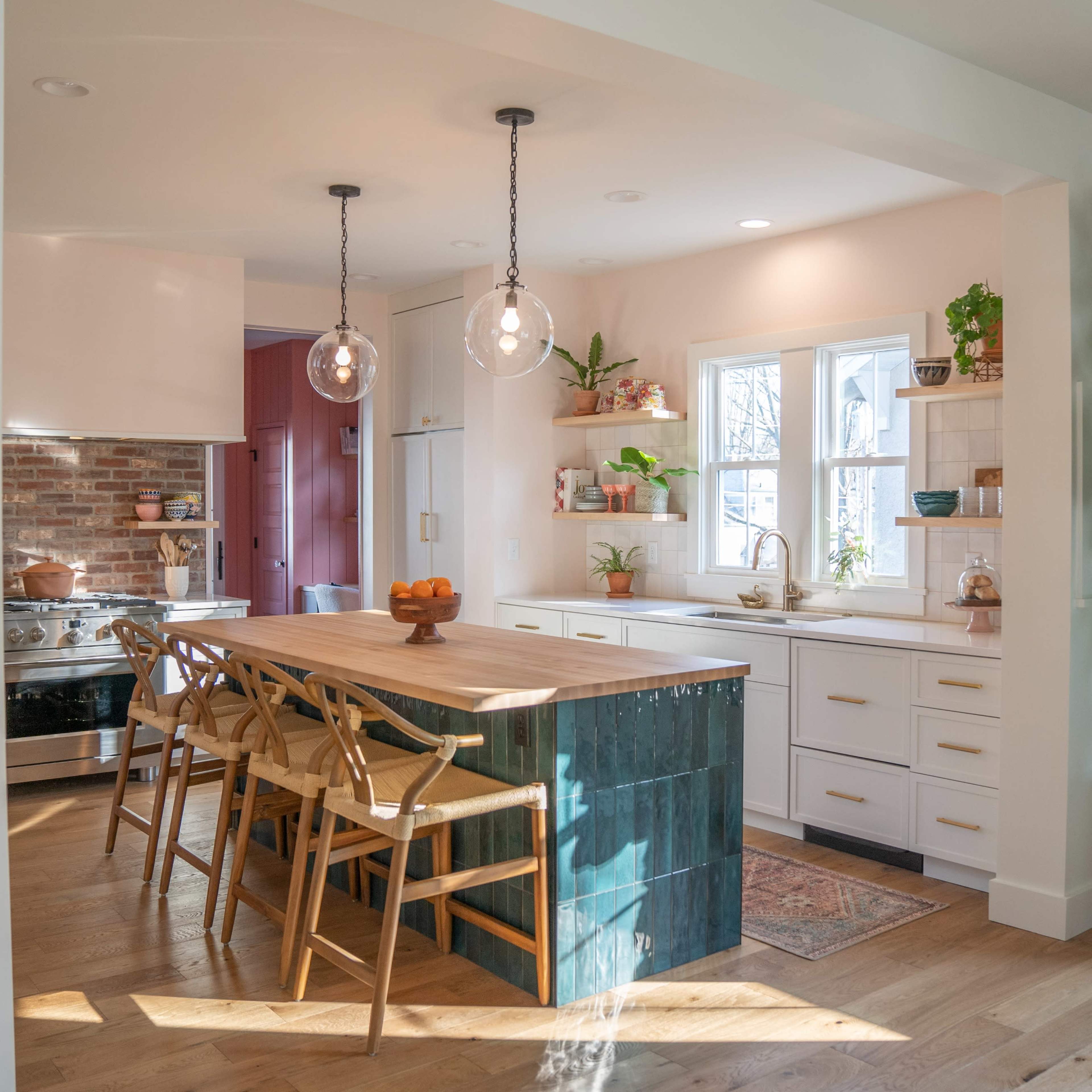 A modern kitchen features a large wooden island with seating, white cabinetry, and an accent wall of exposed brick.