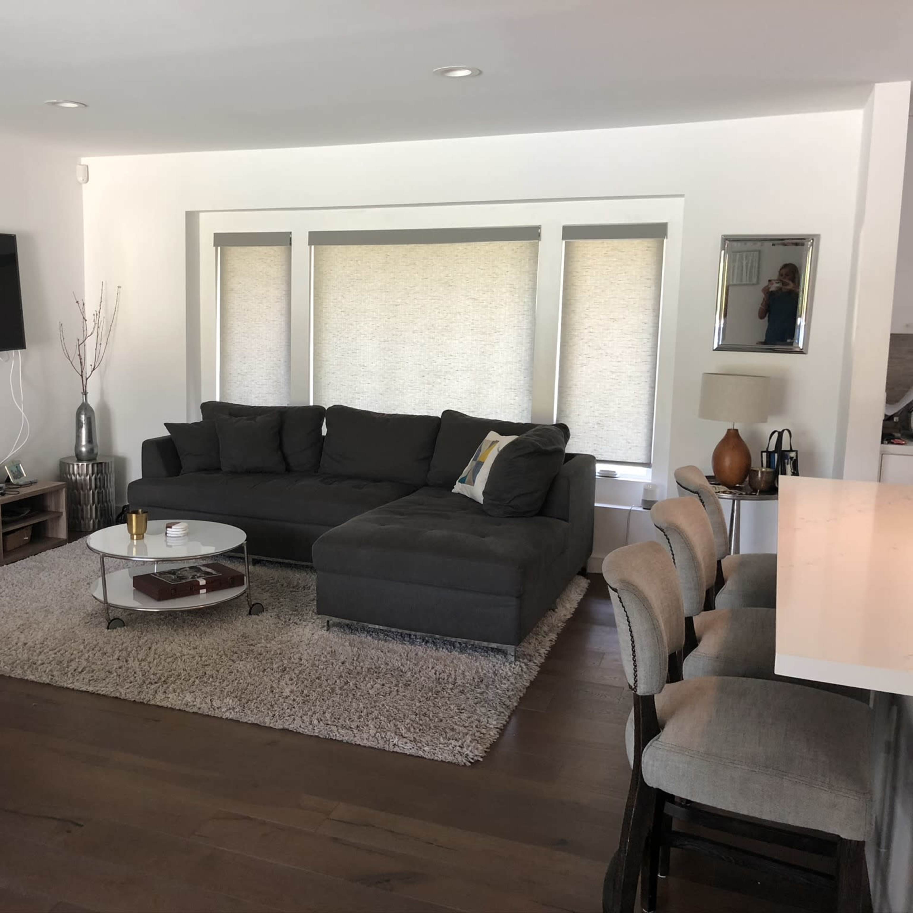 A modern living room with a gray sectional sofa, a circular glass coffee table, and a wall-mounted television.