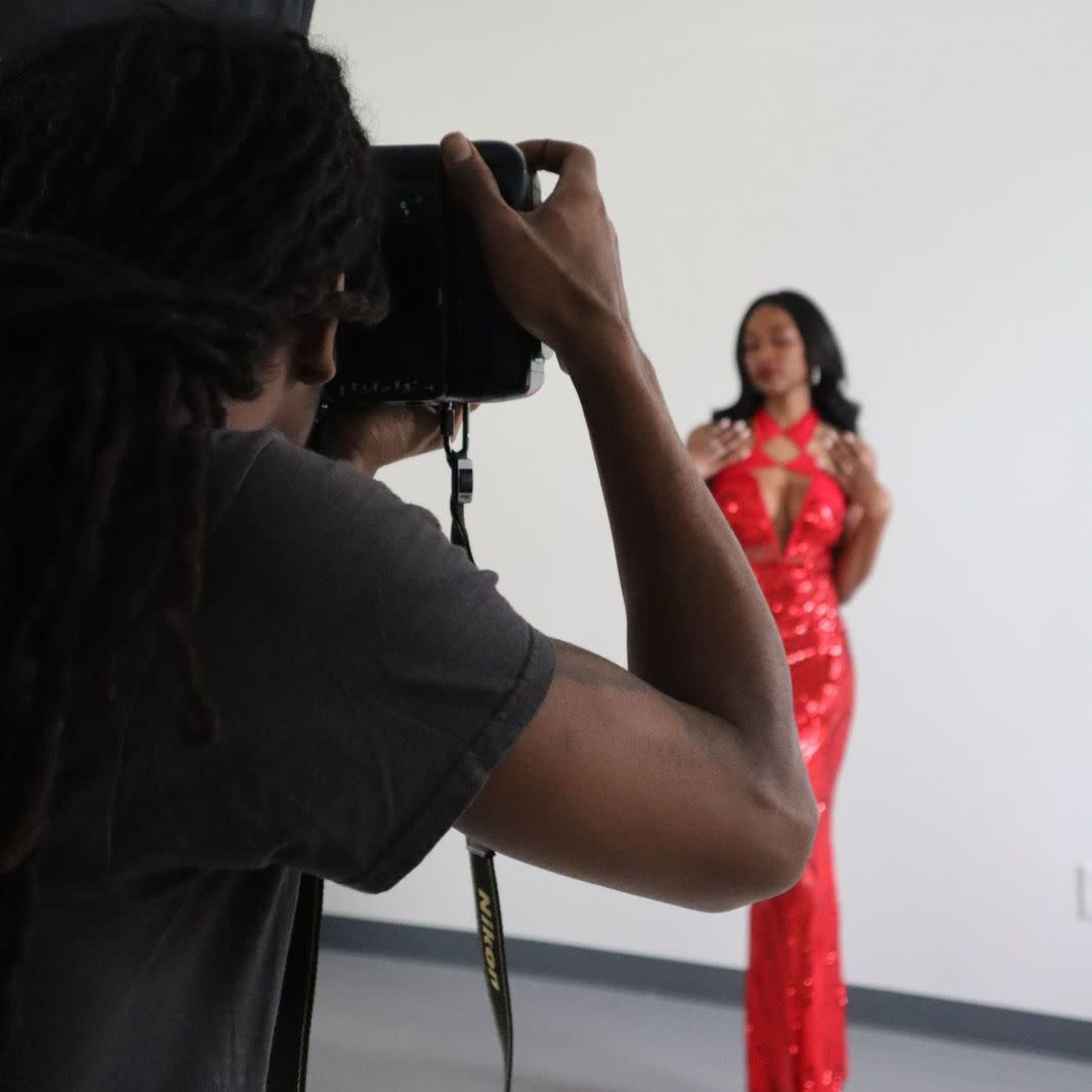 A photographer captures an image of a model wearing a red sequined dress in a studio setting.