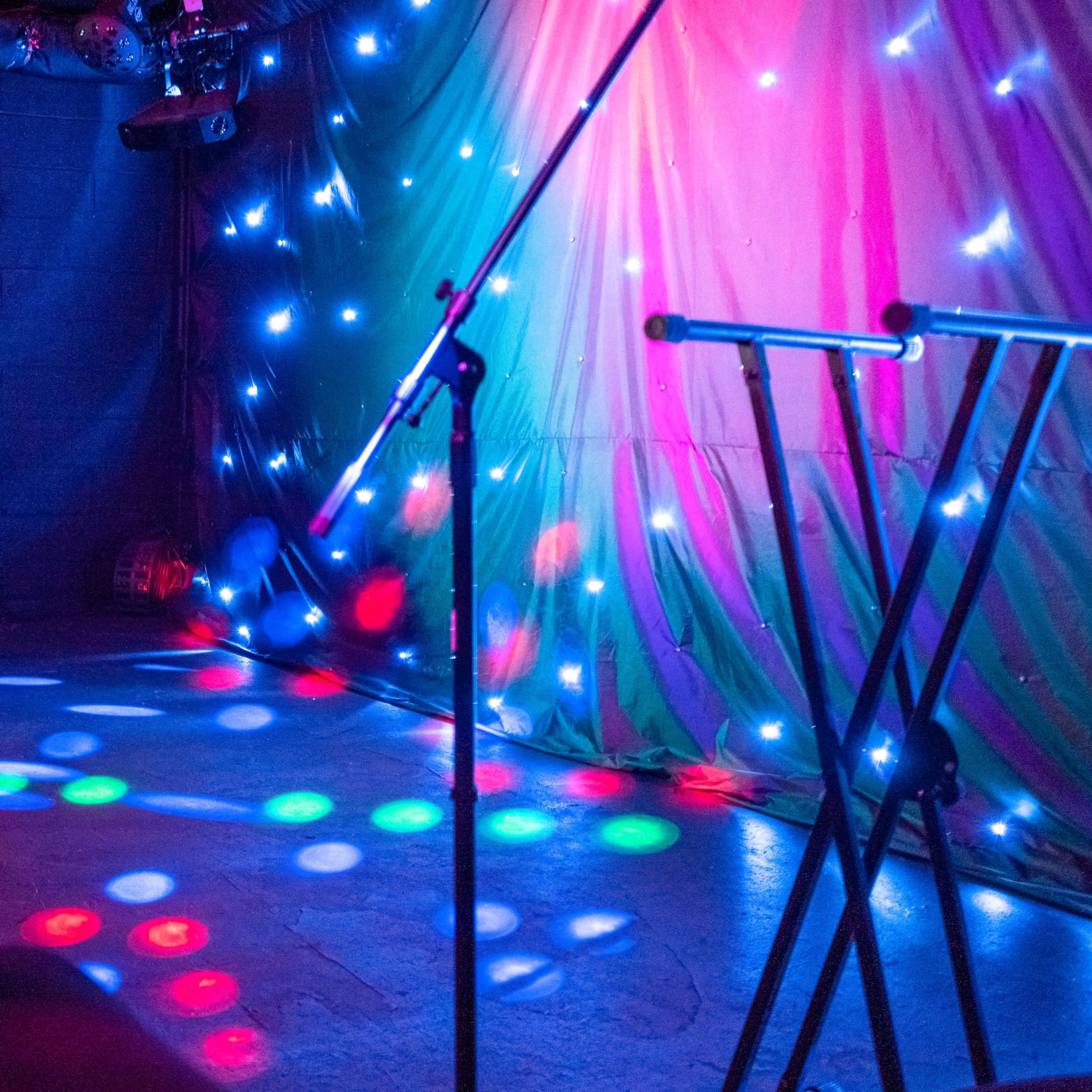A dimly lit stage featuring colorful lights and microphone stands set up for a performance.