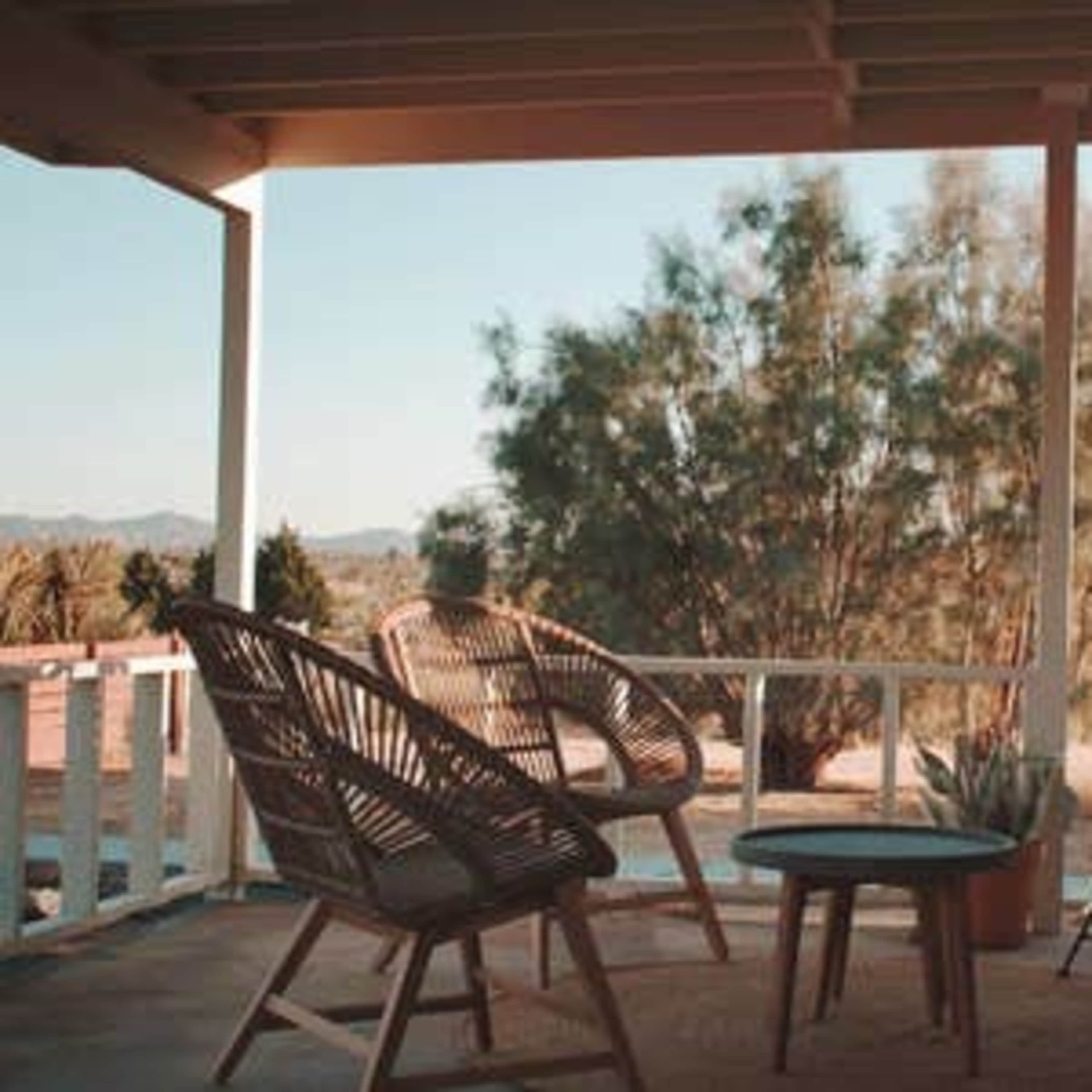 A porch features two rattan chairs and a small table surrounded by desert vegetation.