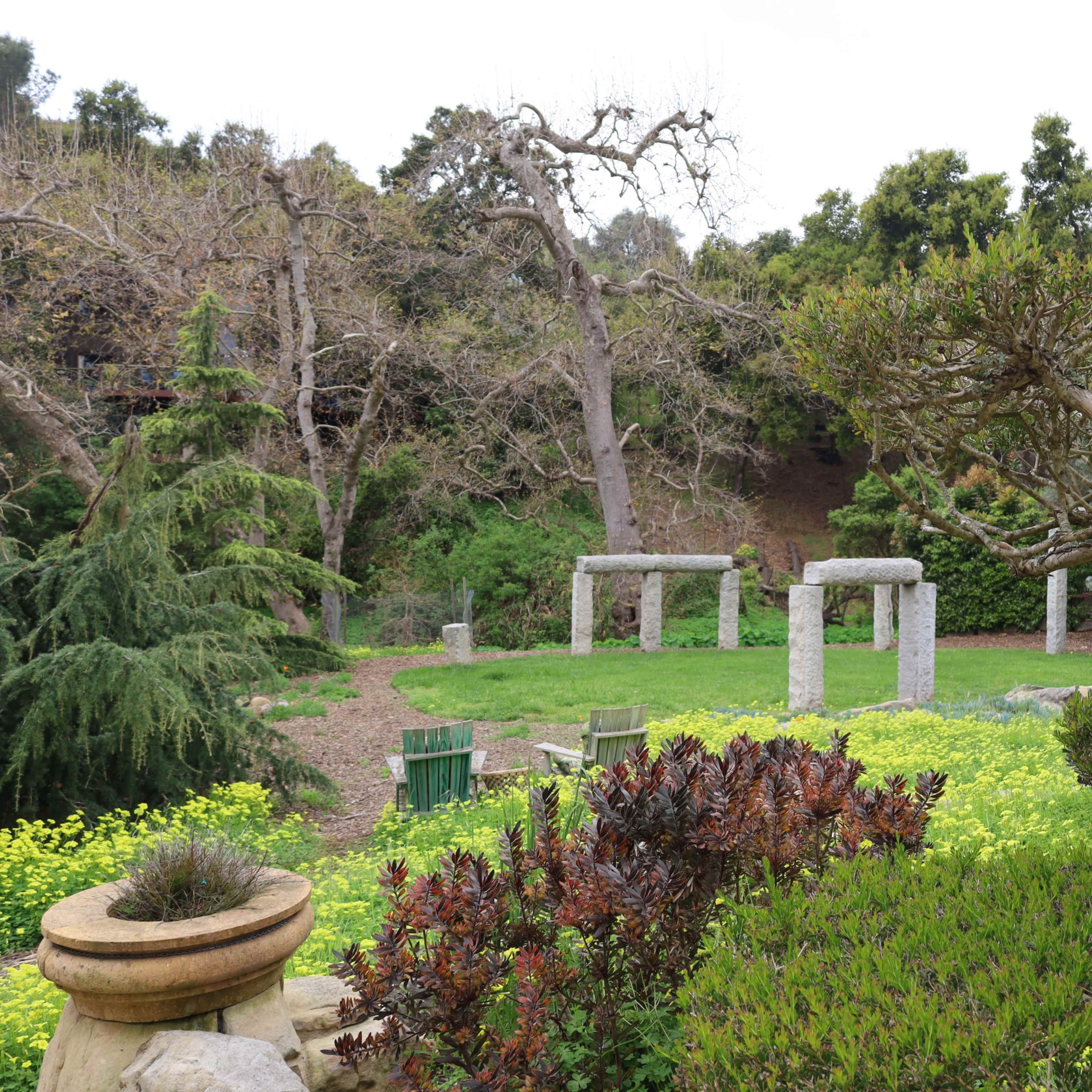 A serene garden with stone columns surrounded by lush greenery and a variety of plants.