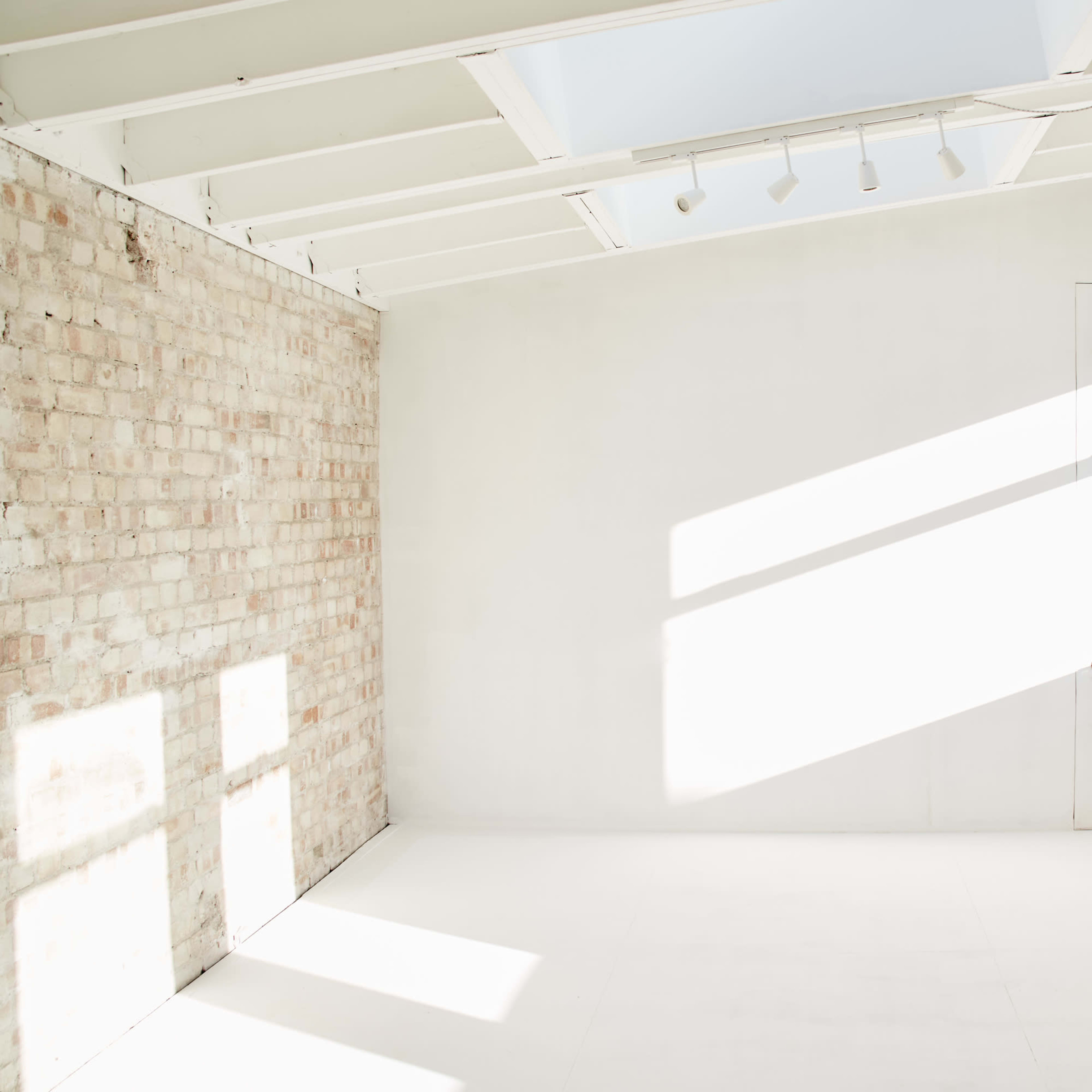 A bright, empty room with white walls and a partially brick wall, illuminated by natural light from a window.