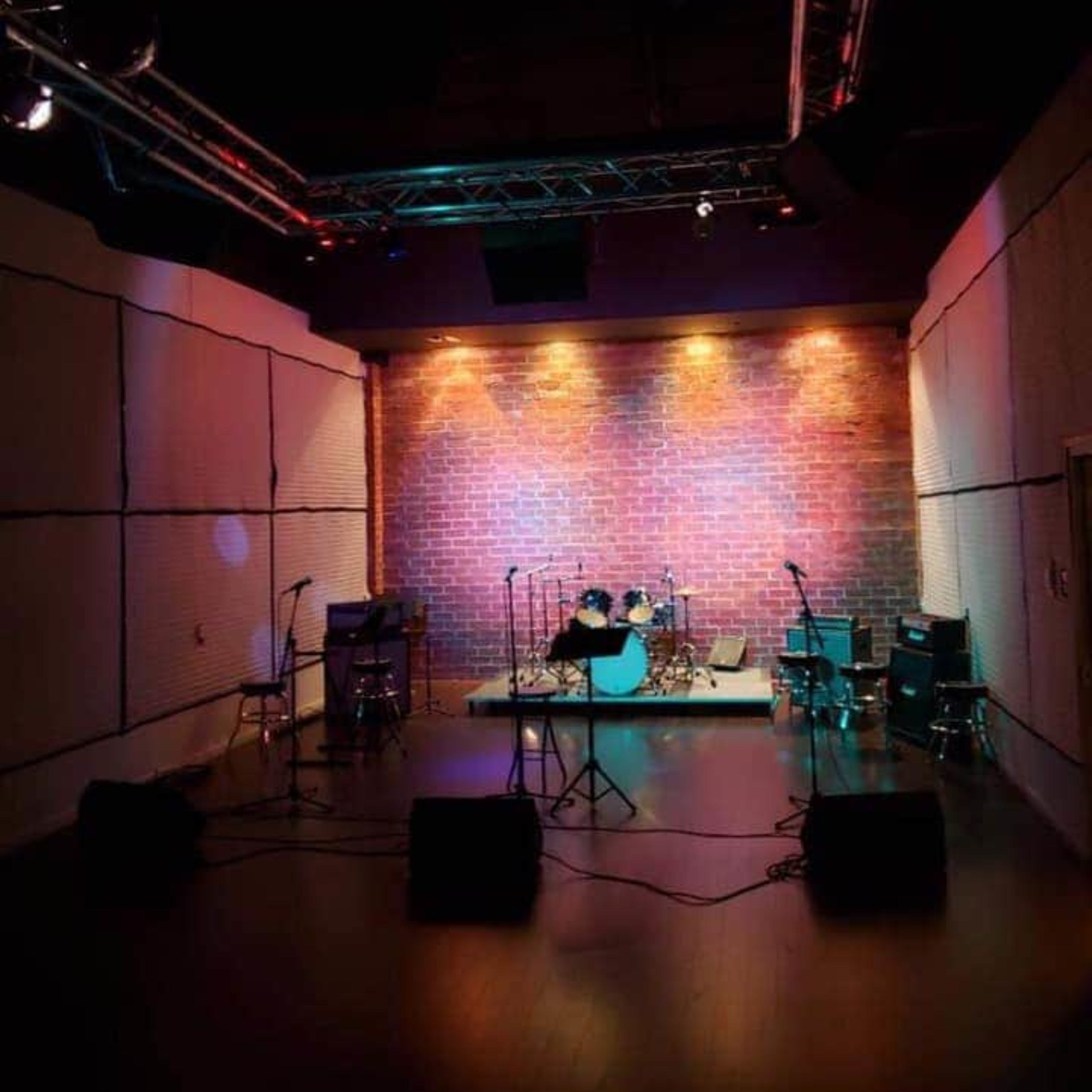 A dimly lit music stage with a brick wall backdrop, equipped with musical instruments and amplified speakers.