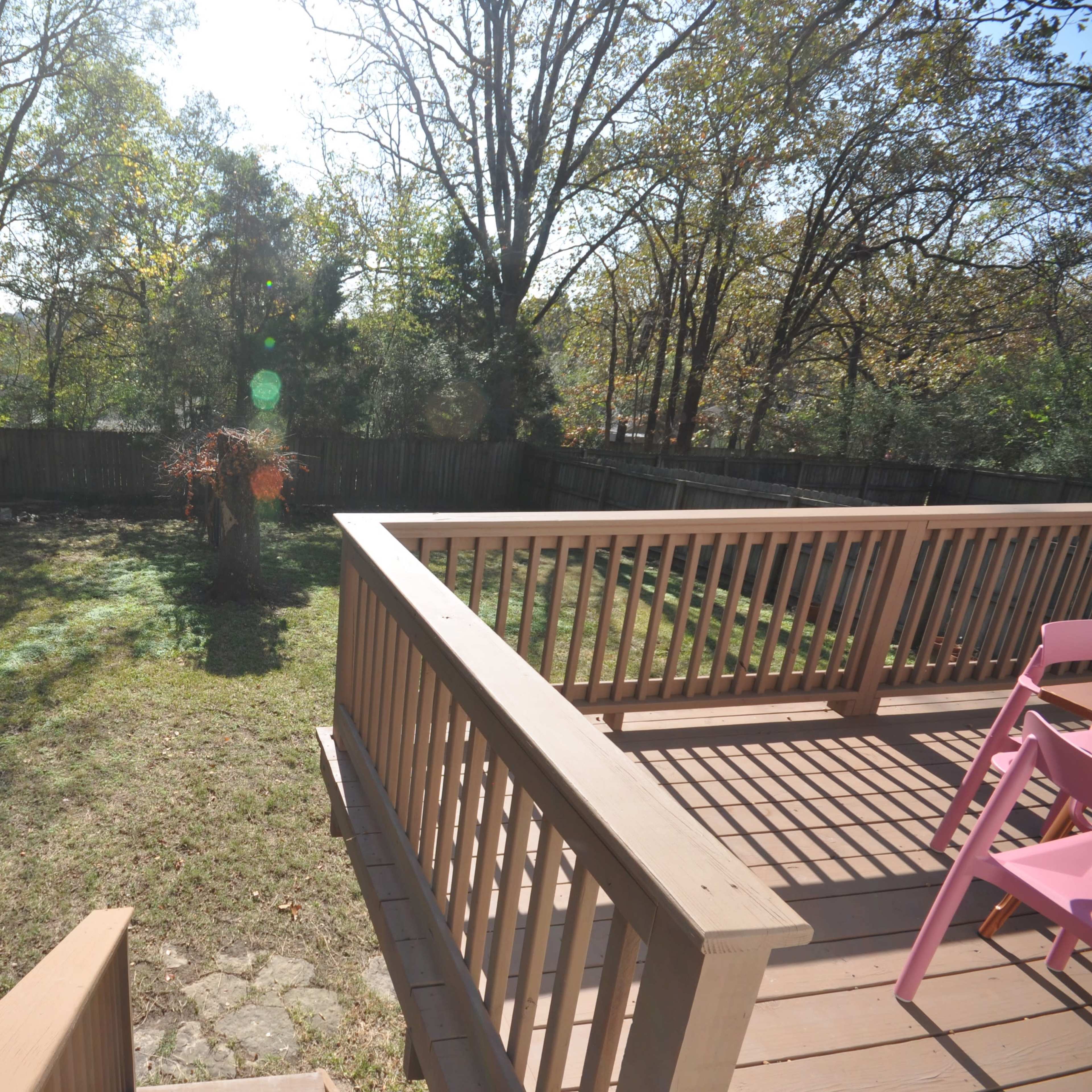 A wooden deck overlooks a grassy backyard surrounded by a wooden fence and trees.