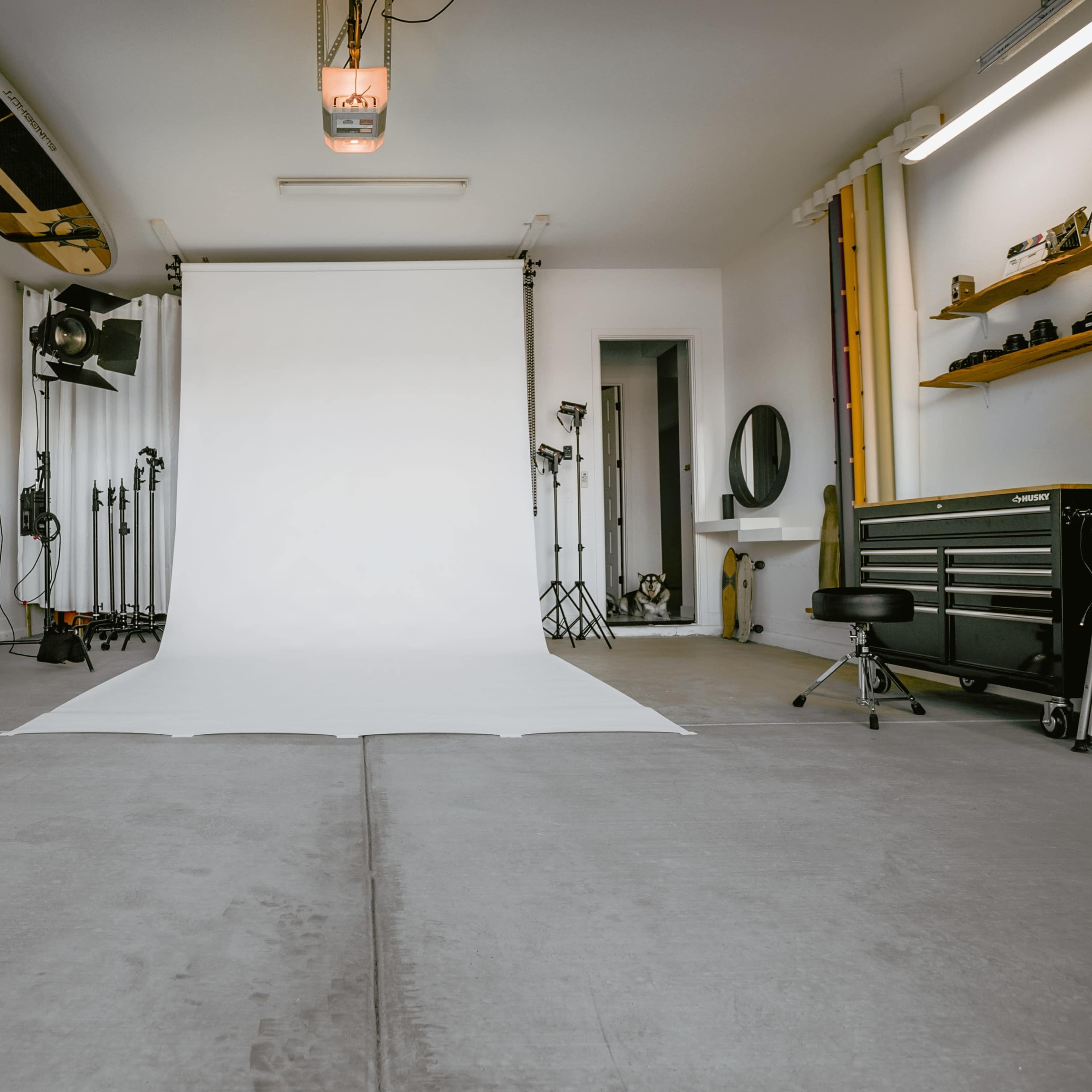 A photography studio features a white backdrop, professional lighting equipment, and various props neatly arranged around the space.