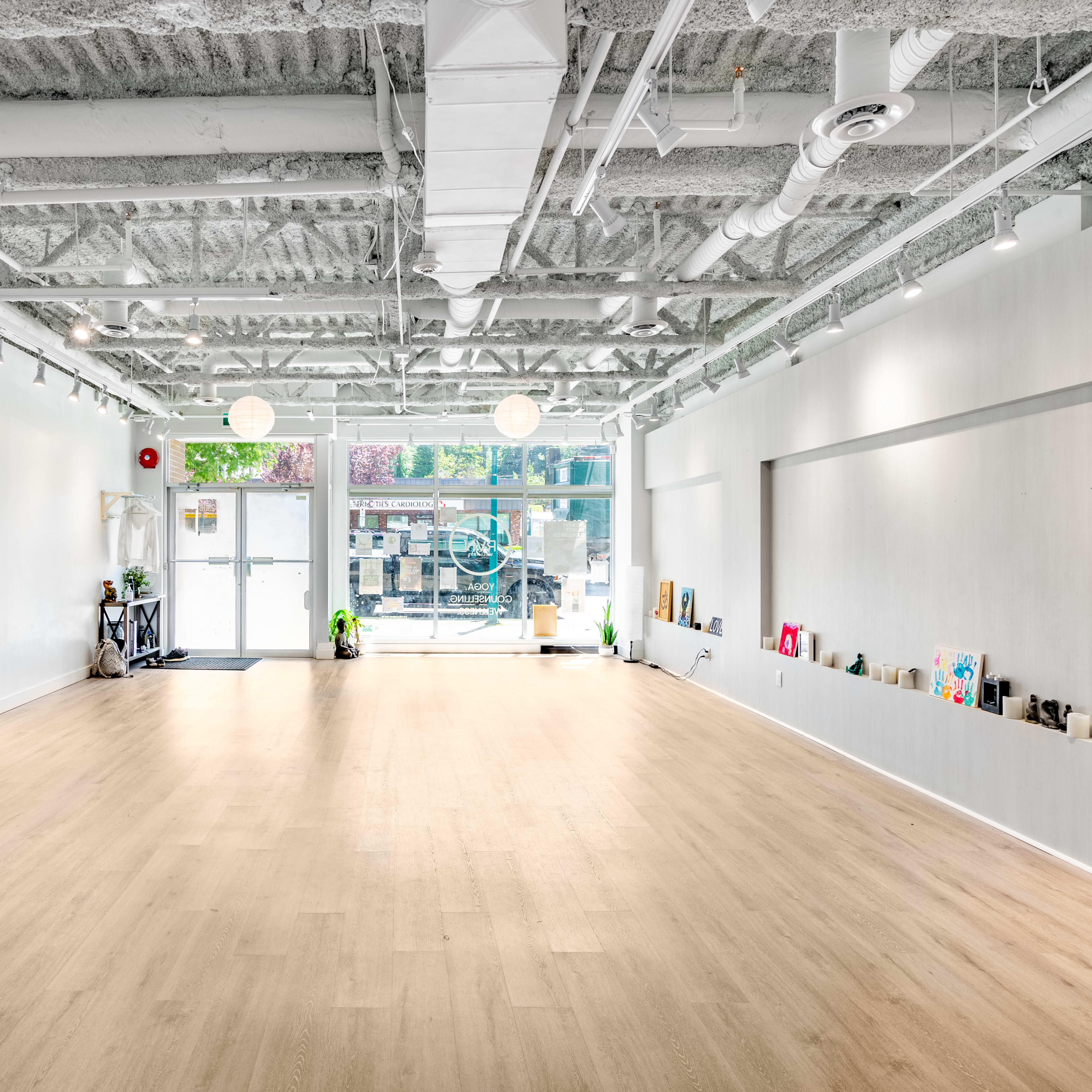 A spacious, empty interior of a modern studio with white walls and wooden flooring, illuminated by natural light from large windows.