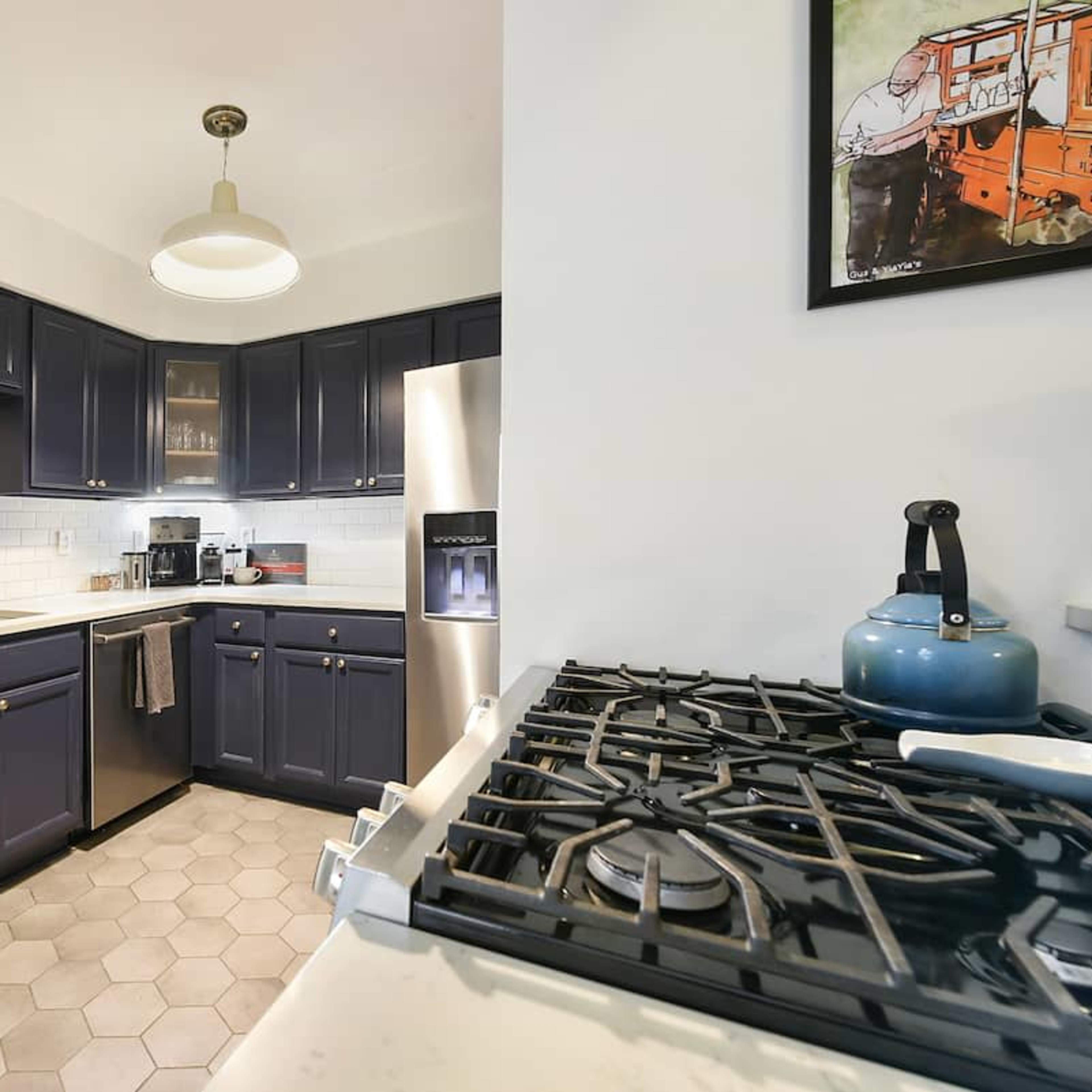 A kitchen with navy blue cabinets, a white tiled backsplash, and a stainless steel refrigerator.