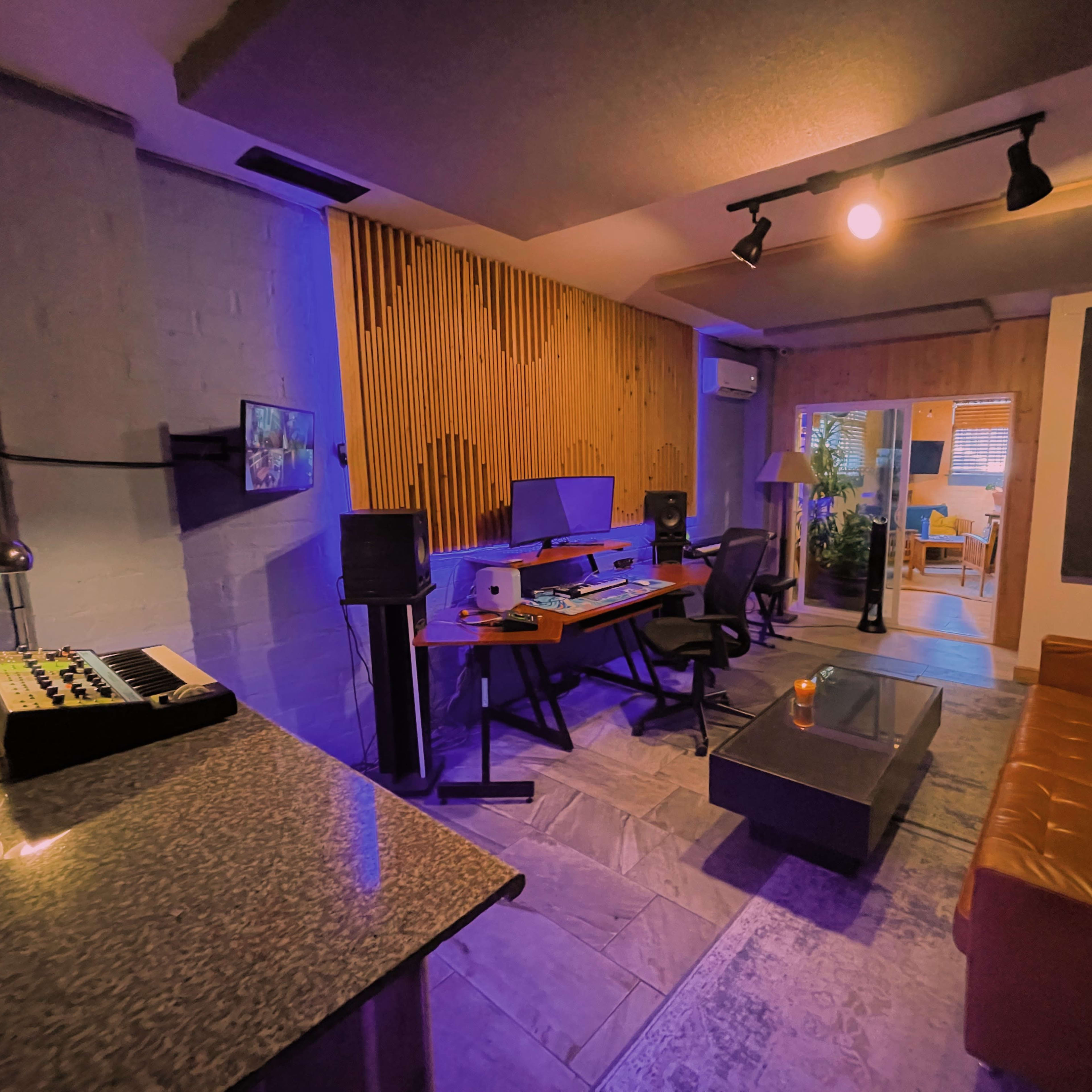 A modern music studio with wooden paneling, a computer setup, and a brown leather sofa.