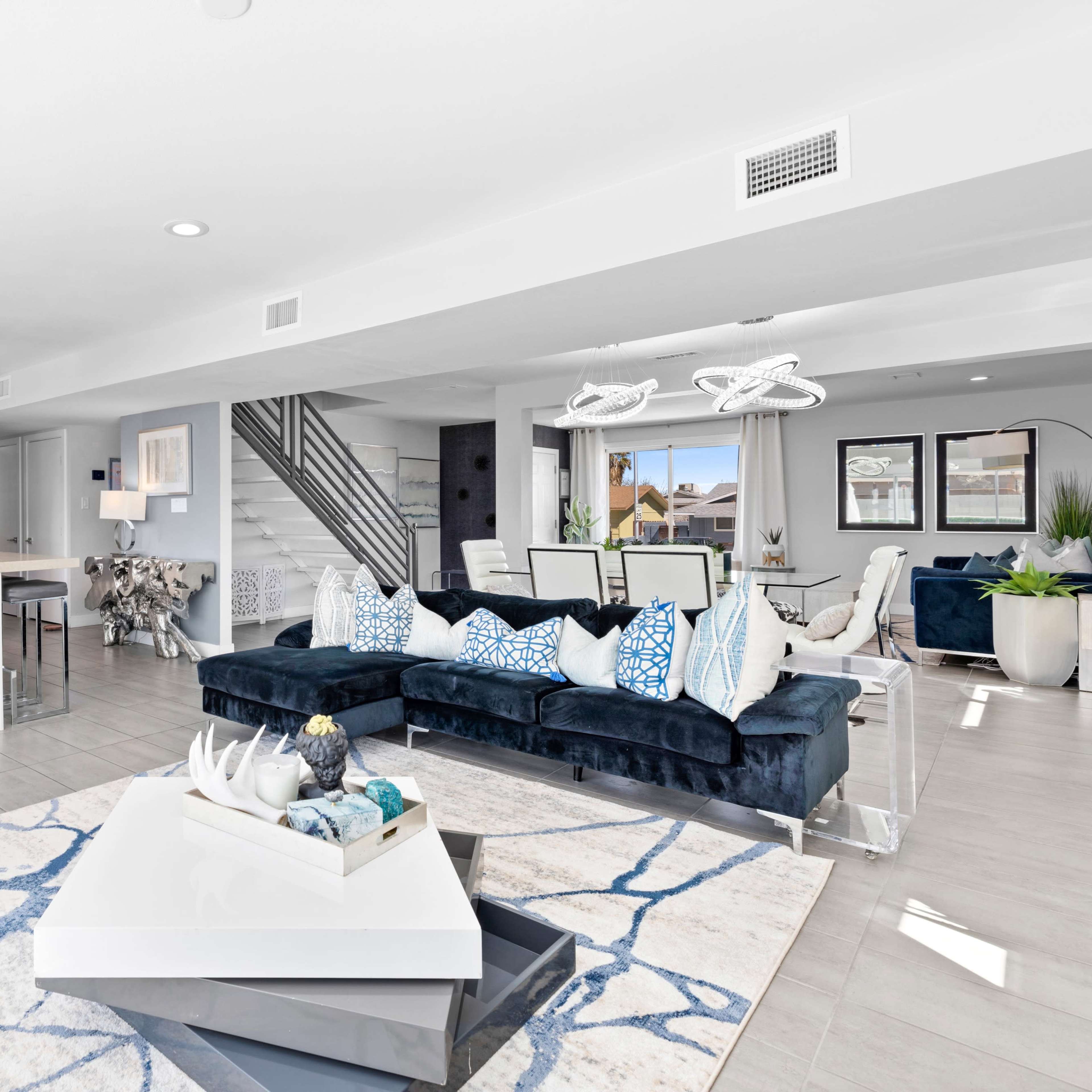 A modern open-concept living space features a dark blue sectional sofa, a coffee table with decorative items, and a stylish accent wall with tropical foliage.