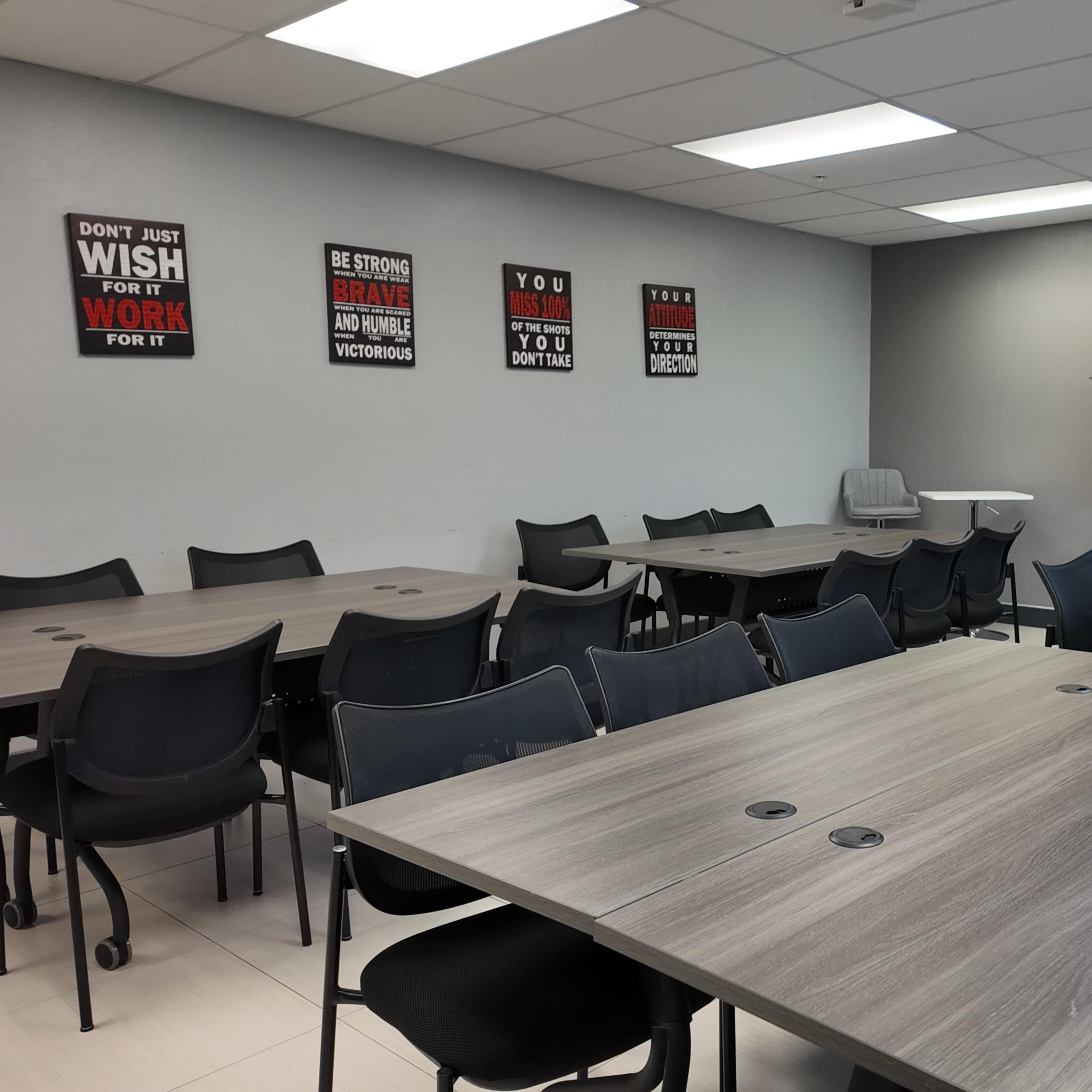A modern conference room with multiple tables and chairs arranged neatly, along with motivational posters on the wall and a large screen at the front.