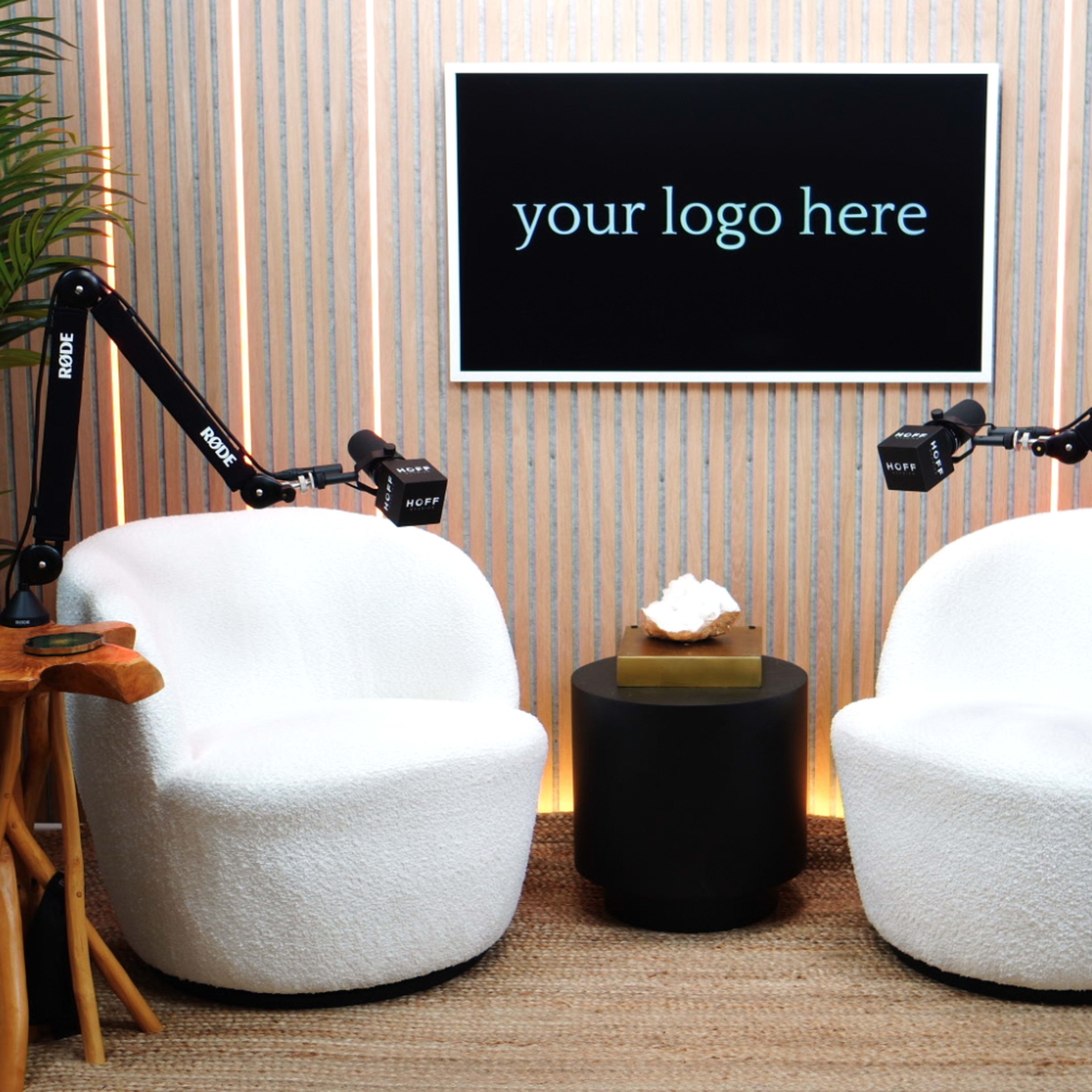 A cozy seating area features two white chairs with wooden side tables, illuminated by a softly lit backdrop with a space for a logo.