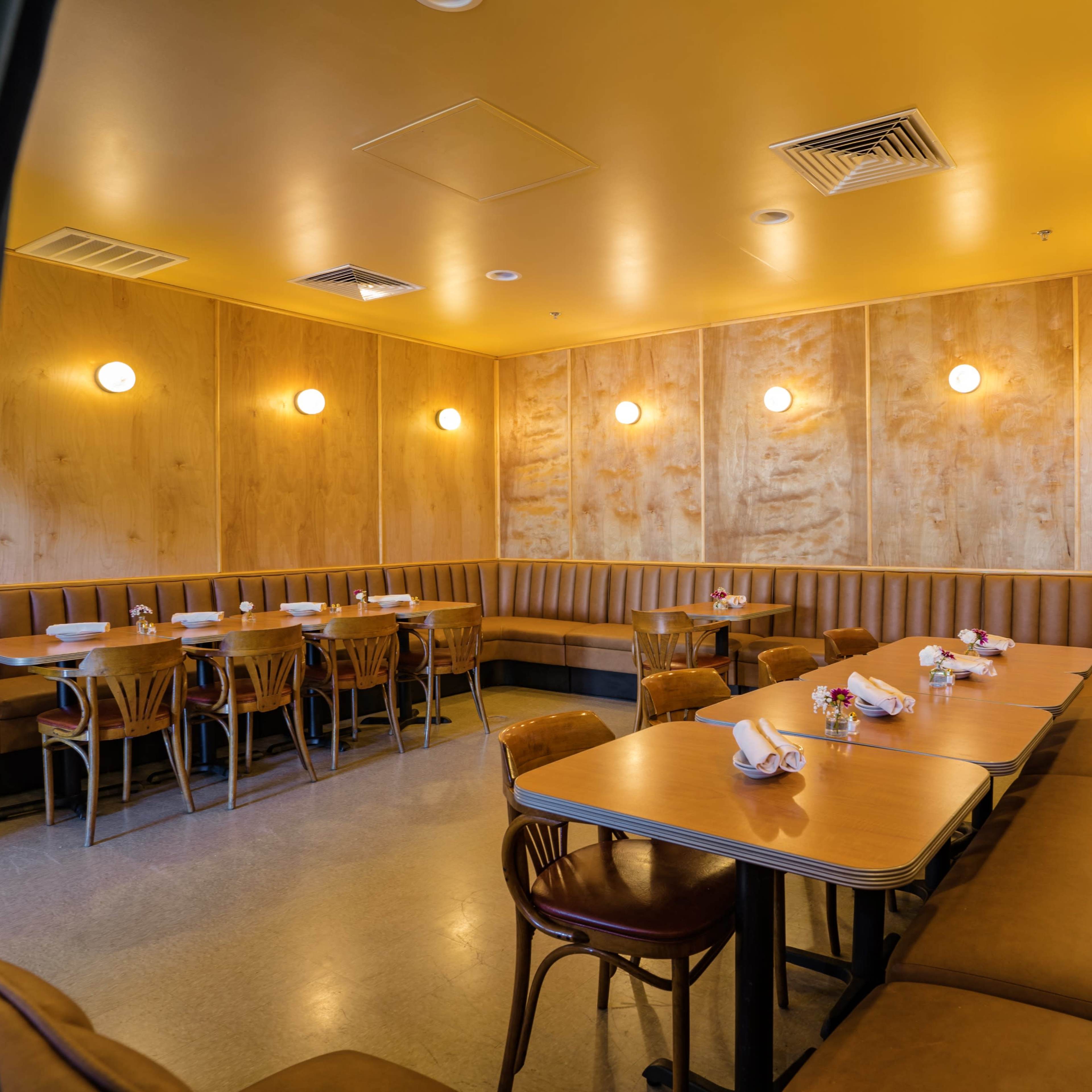 A modern restaurant interior with wooden paneling, neatly set tables, and cozy booth seating arranged against the walls.