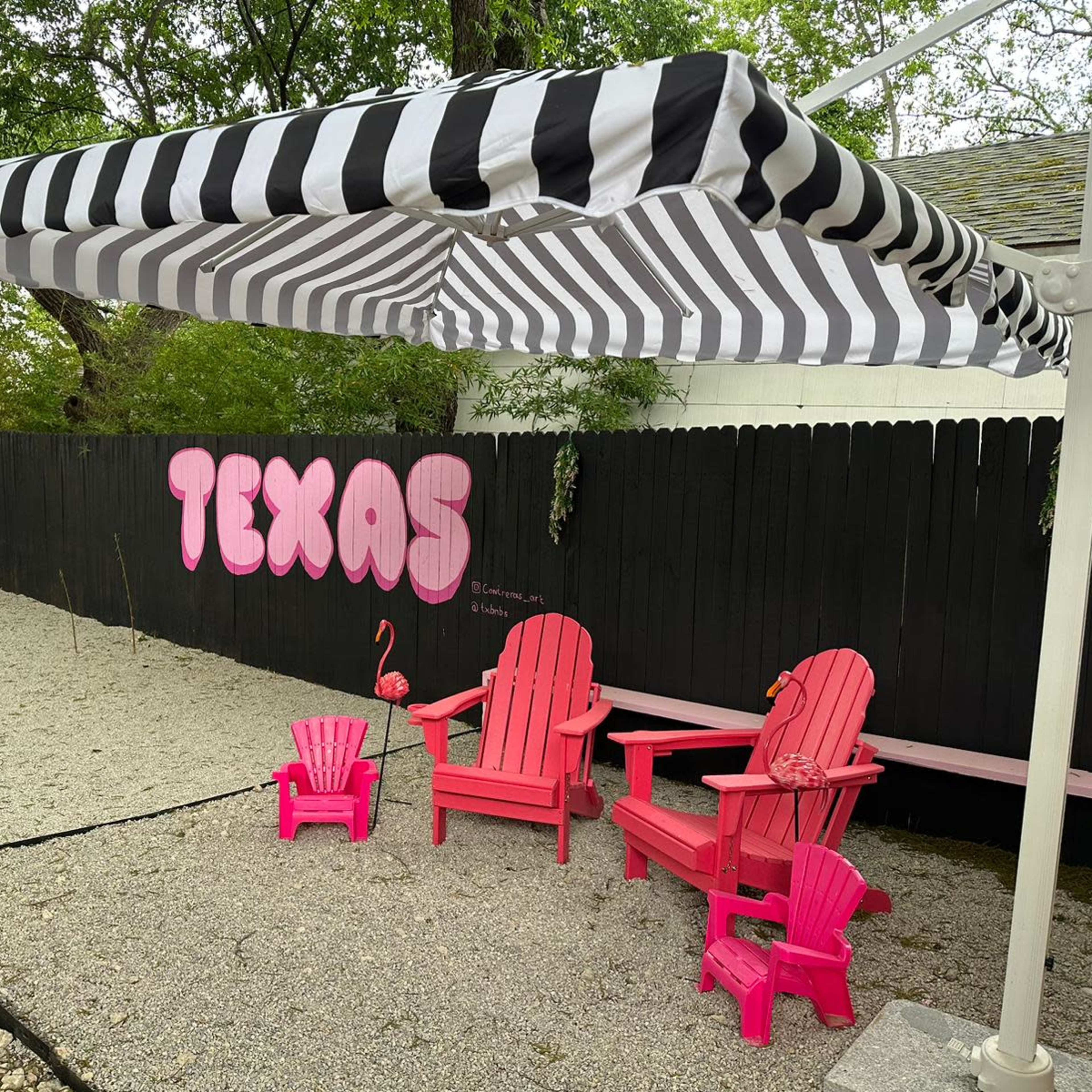 A shaded area features pink Adirondack chairs and a flamingo statue in front of a black fence with "TEXAS" painted on it.