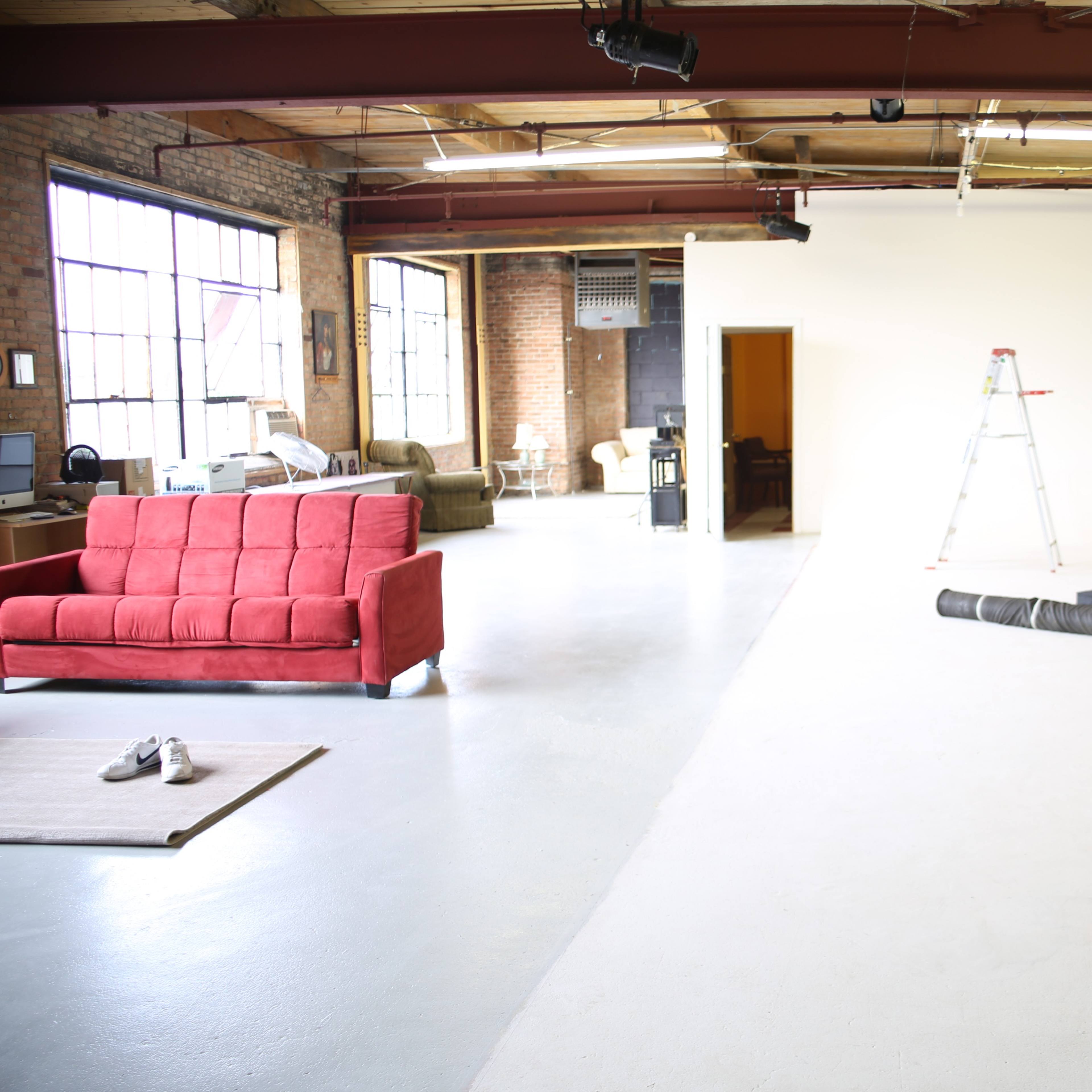 A spacious studio with a red couch, a ladder, lighting equipment, and a backdrop setup for photography.