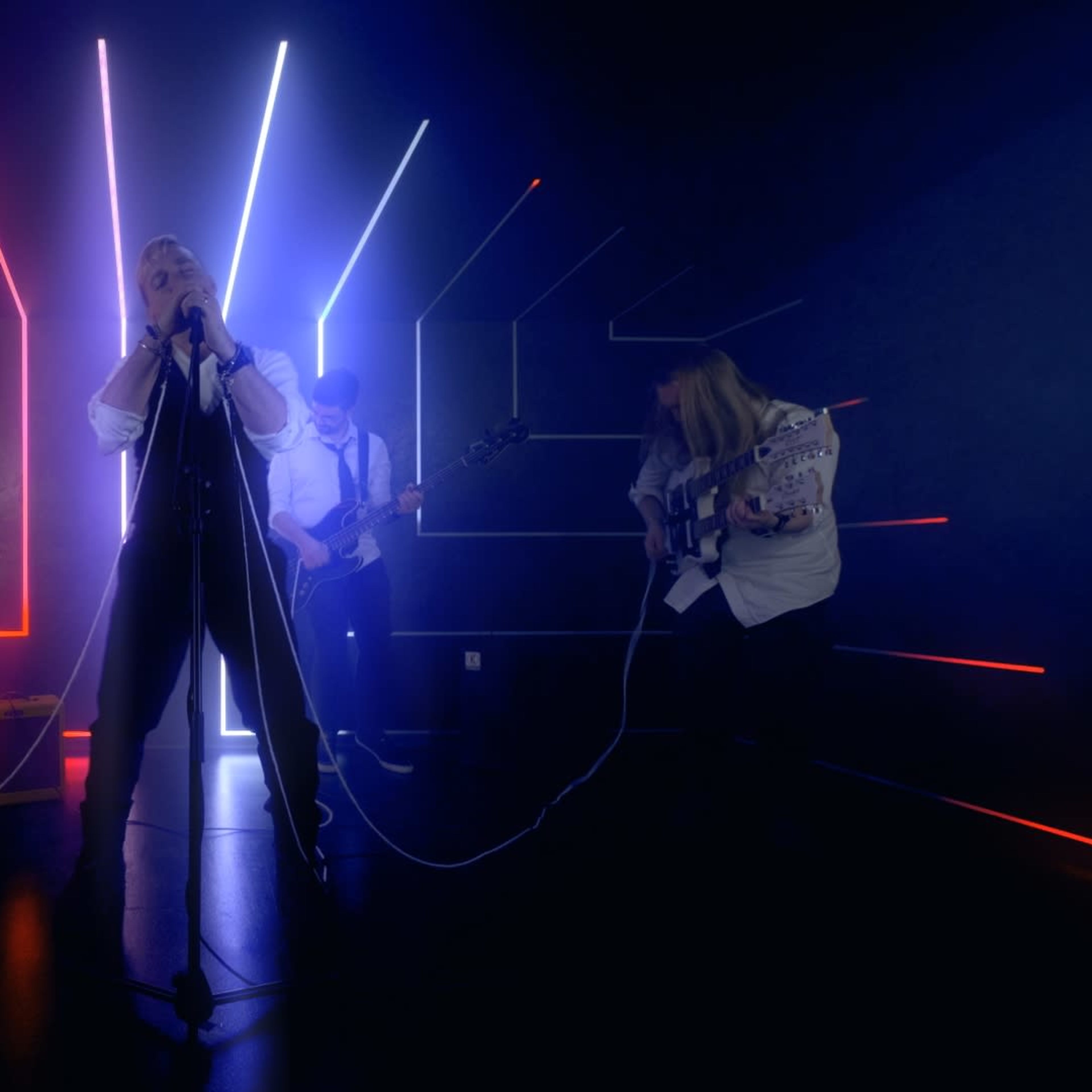 A band performs in a dimly lit space with neon light patterns in red and blue.
