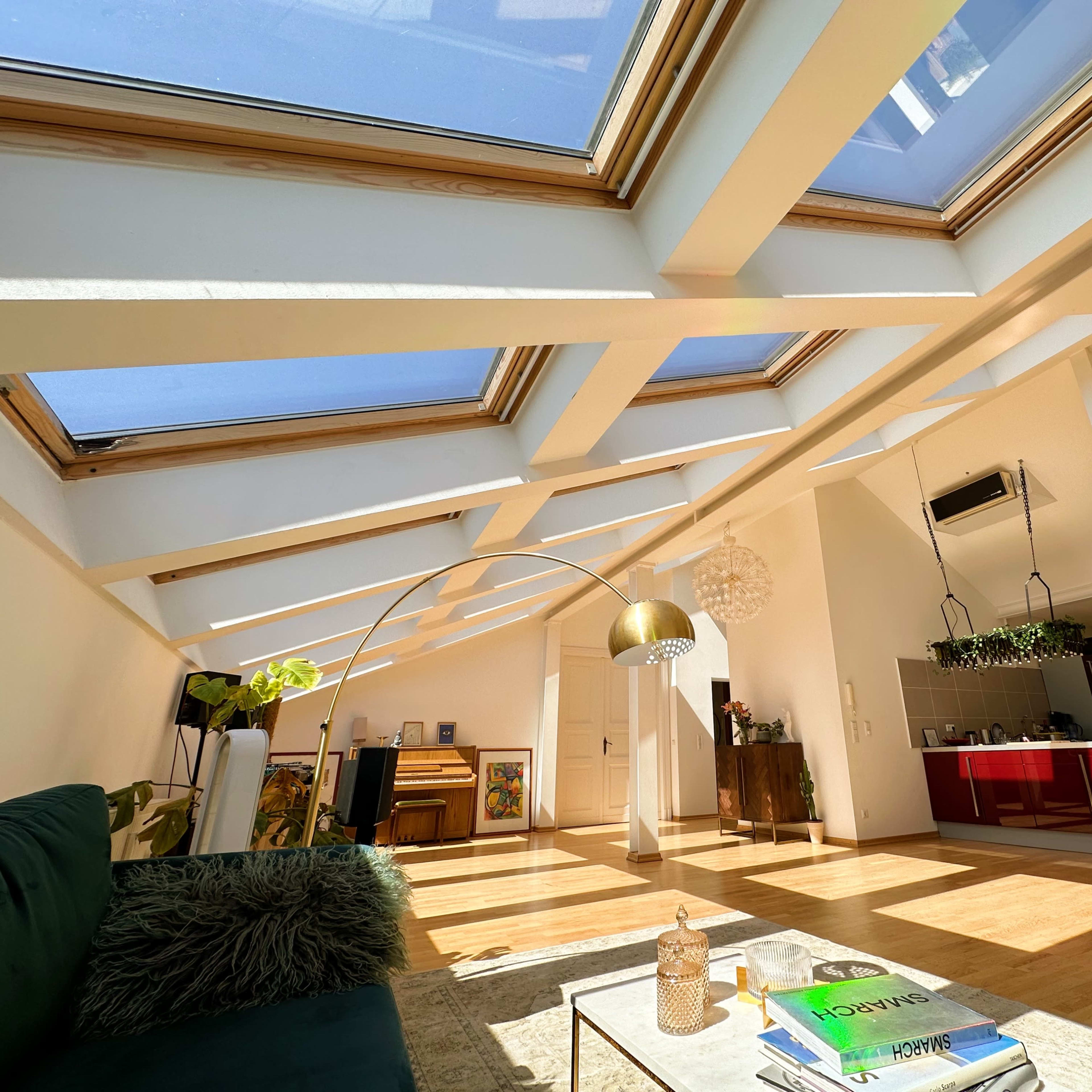 A bright, modern living space with a skylight, featuring a green sofa, a coffee table, and a view into a kitchen area.