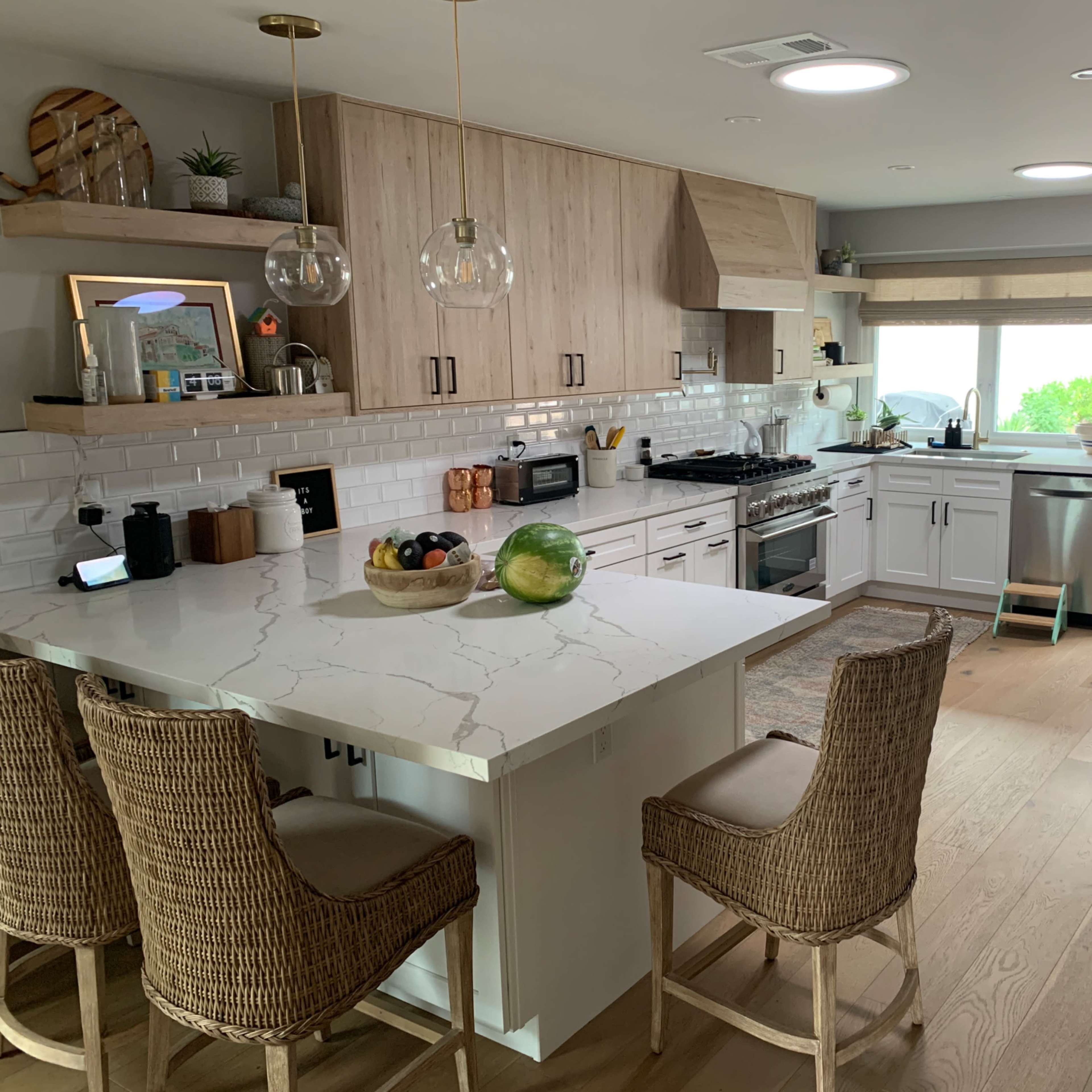 A modern kitchen features white cabinetry, a marble countertop island with bar stools, and large windows allowing natural light.