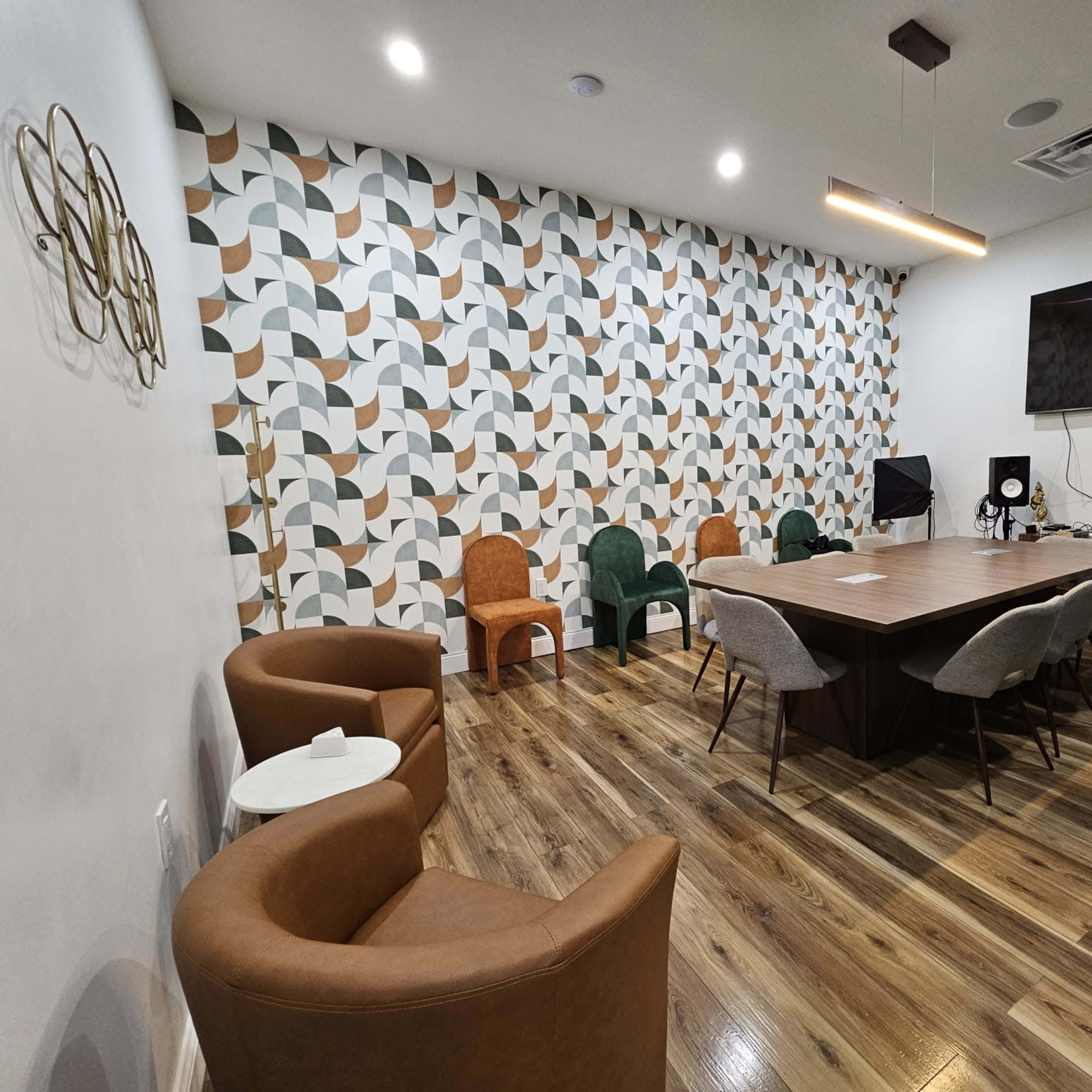 A meeting room with a large wooden table surrounded by various chairs, a television on the wall, and a geometric patterned wallpaper.