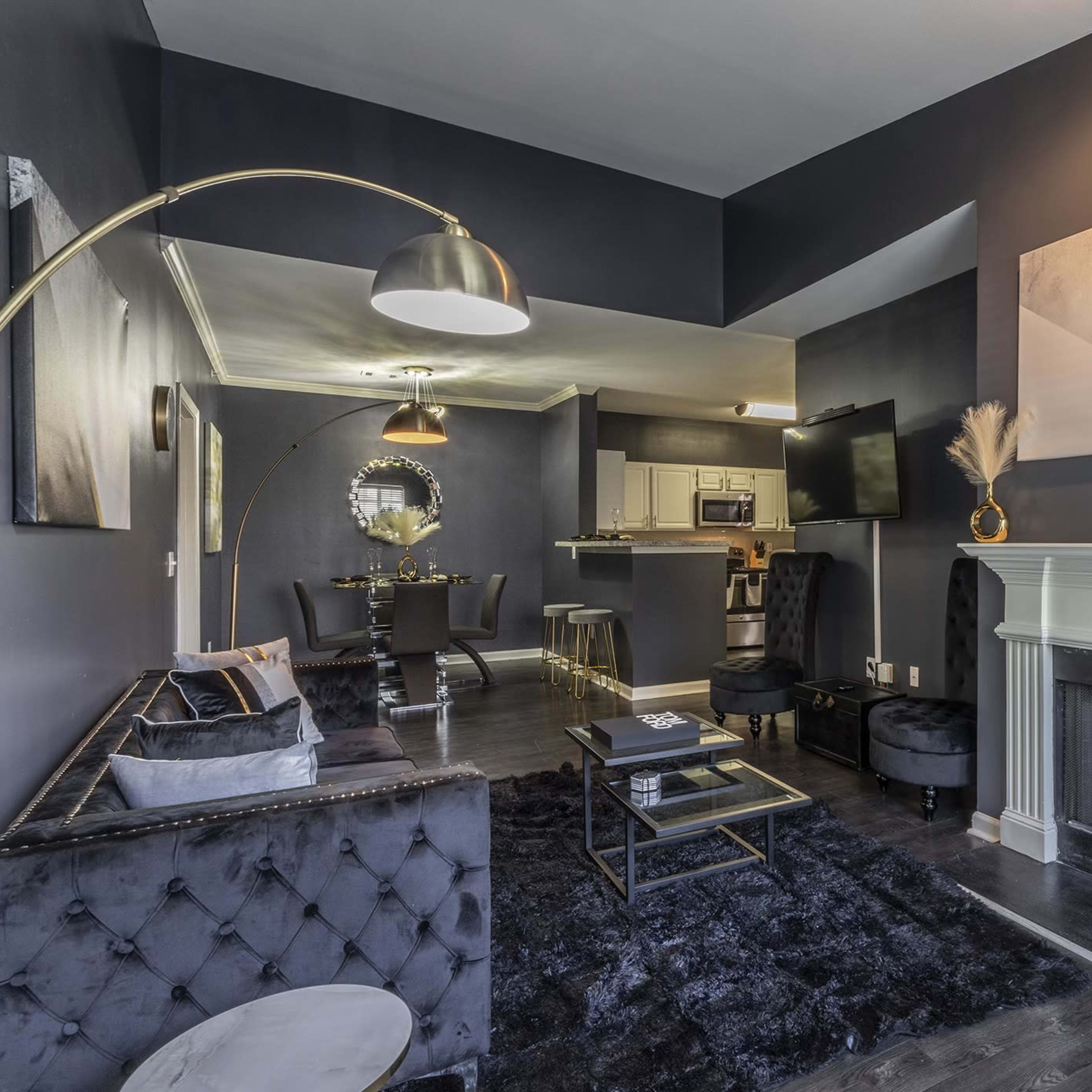 A modern living room with dark walls, a plush rug, a sleek sofa, and a fireplace, leading into an open kitchen and dining area.