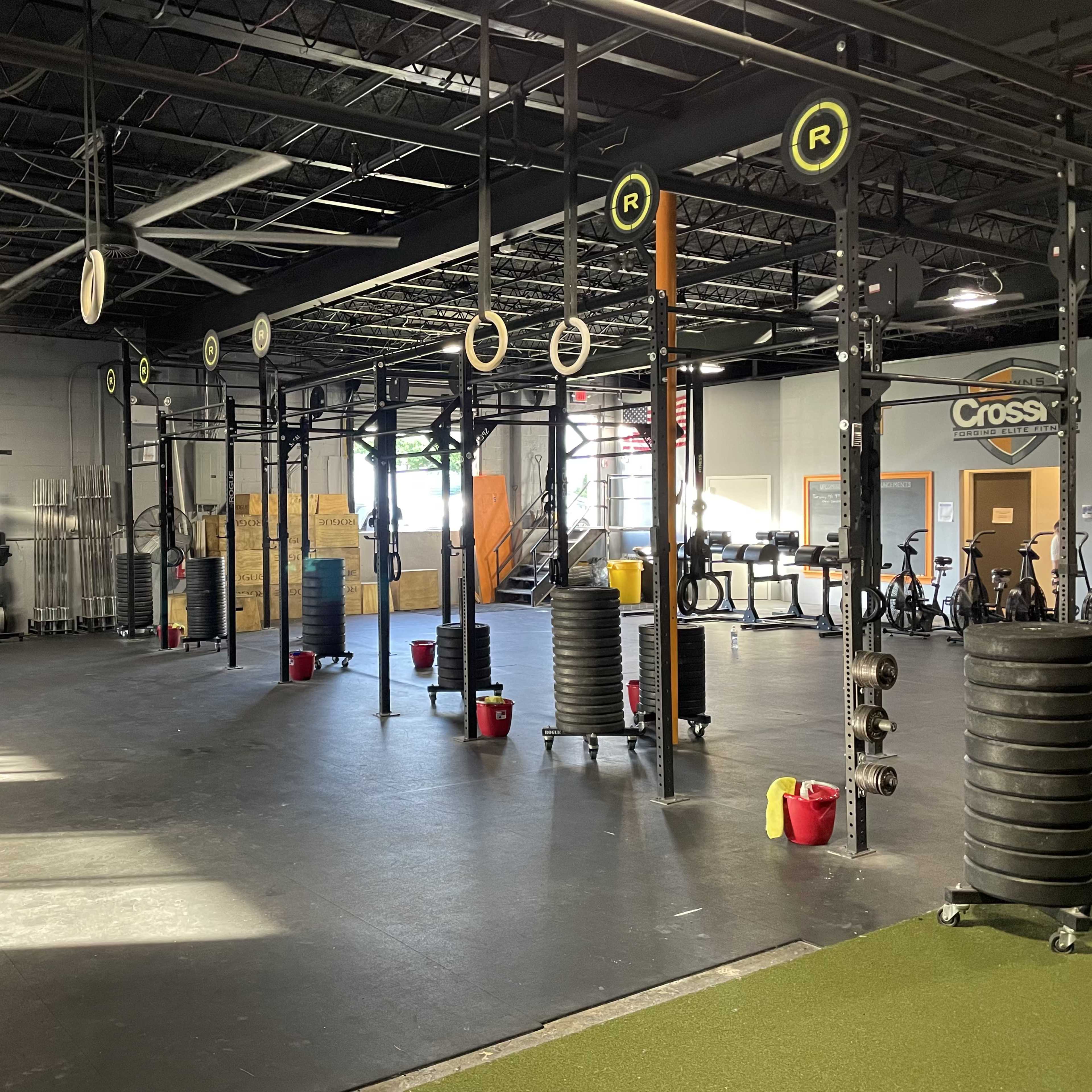 A spacious gym area with weightlifting equipment, exercise mats, and a row of rowing machines along the wall.