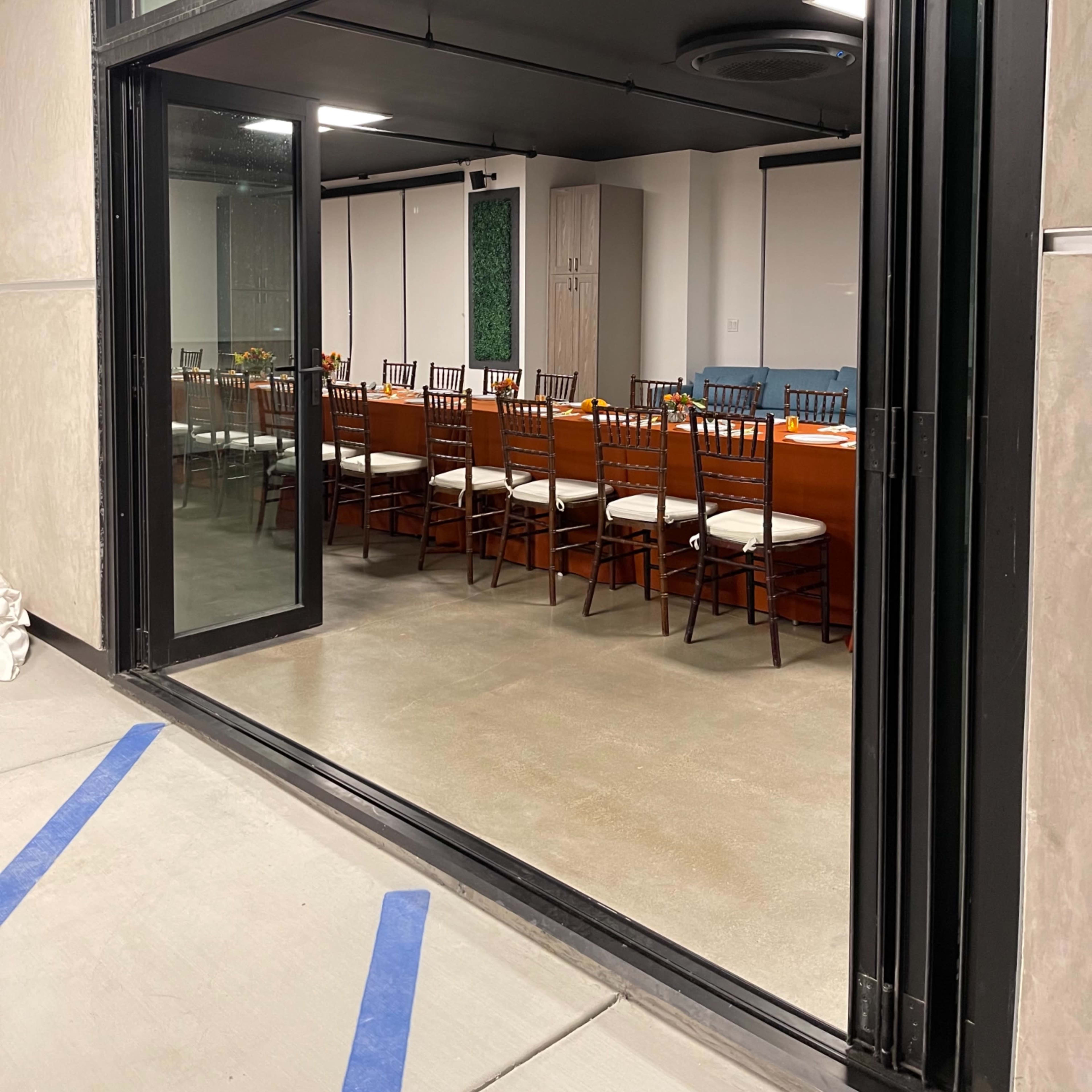 A large meeting room with a long wooden table and multiple chairs, visible through an opened glass sliding door.