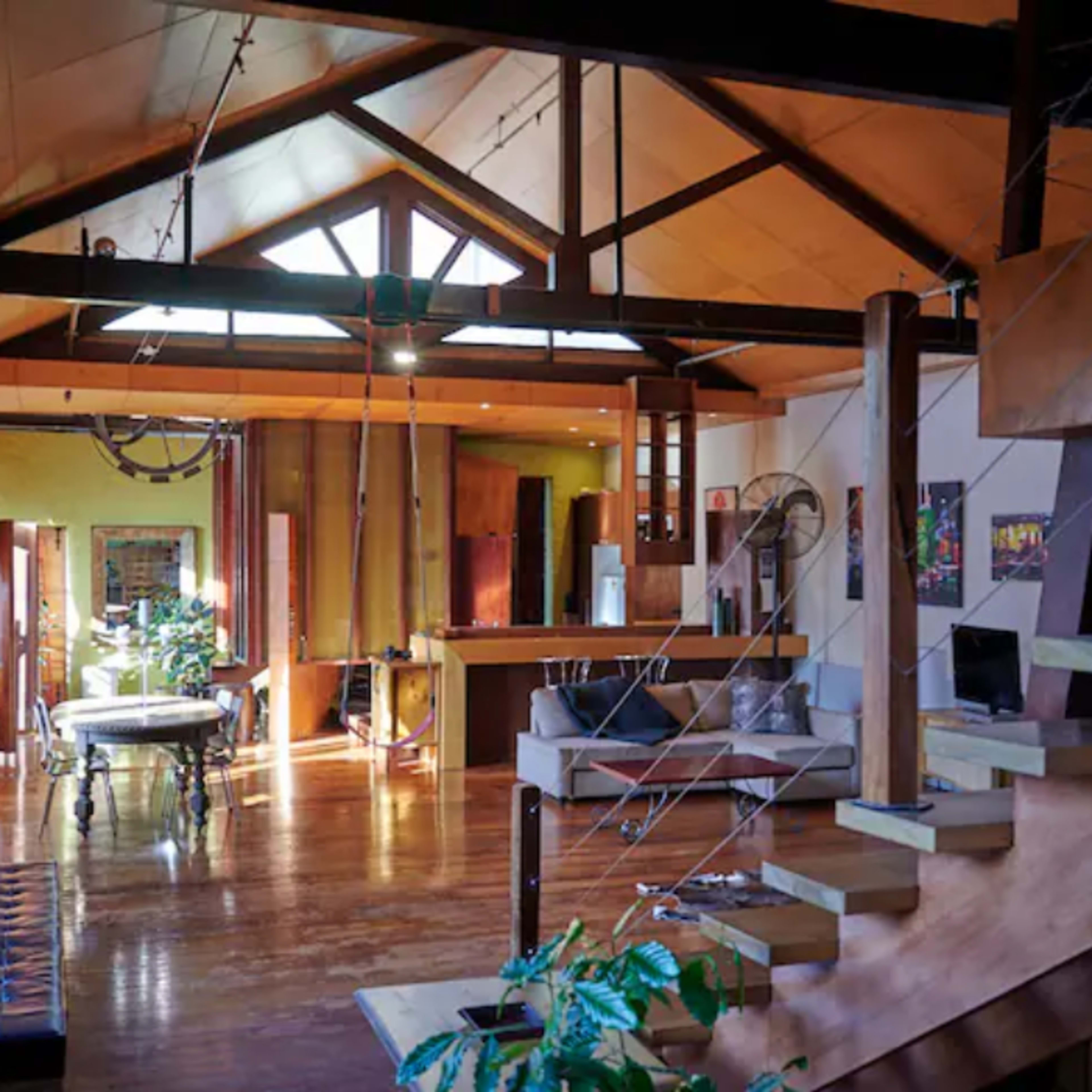 A spacious, open-concept living area with wooden beams, large windows, and a staircase leading to an upper level.