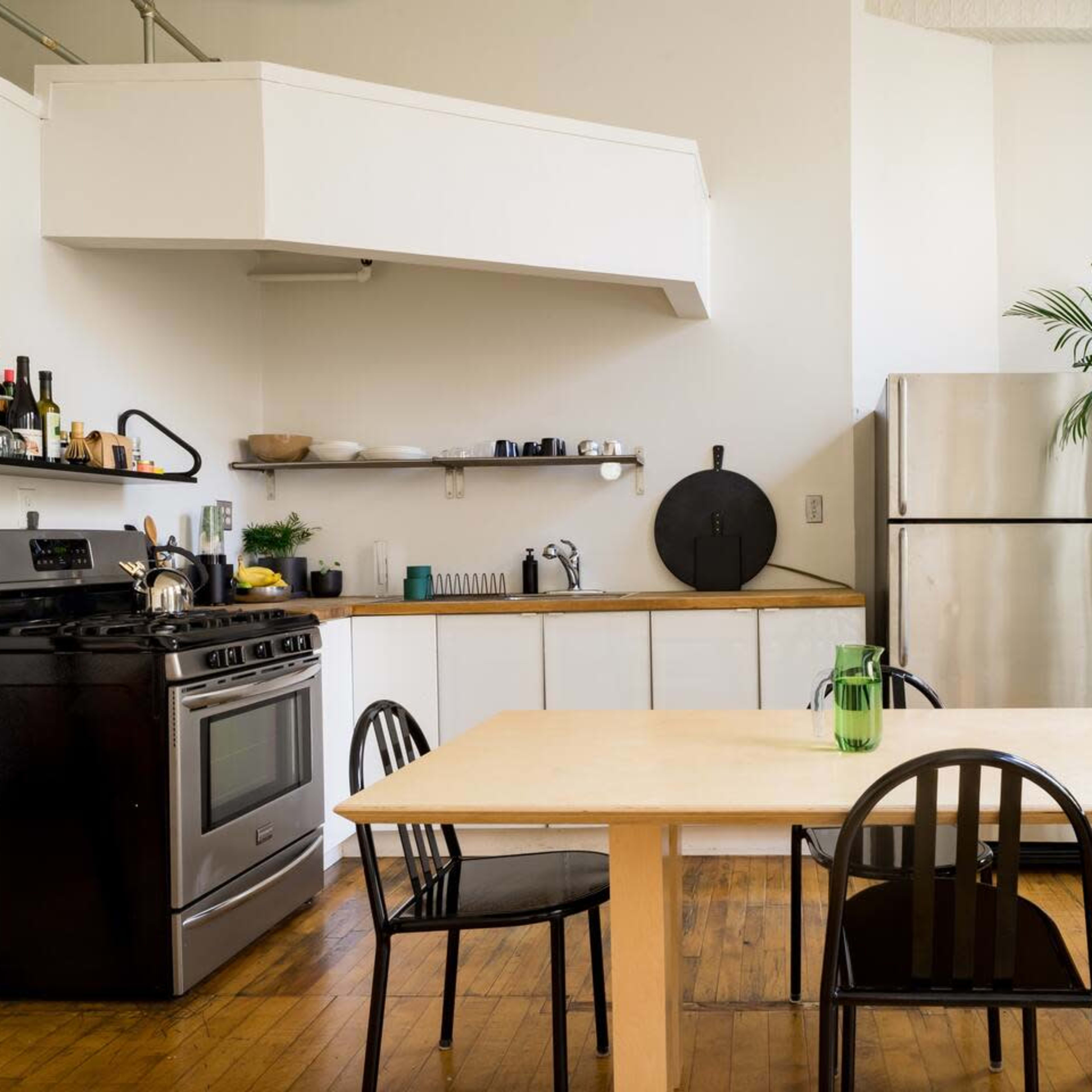 A modern kitchen features a stainless steel refrigerator, a black stove, and a wooden dining table surrounded by four black chairs.