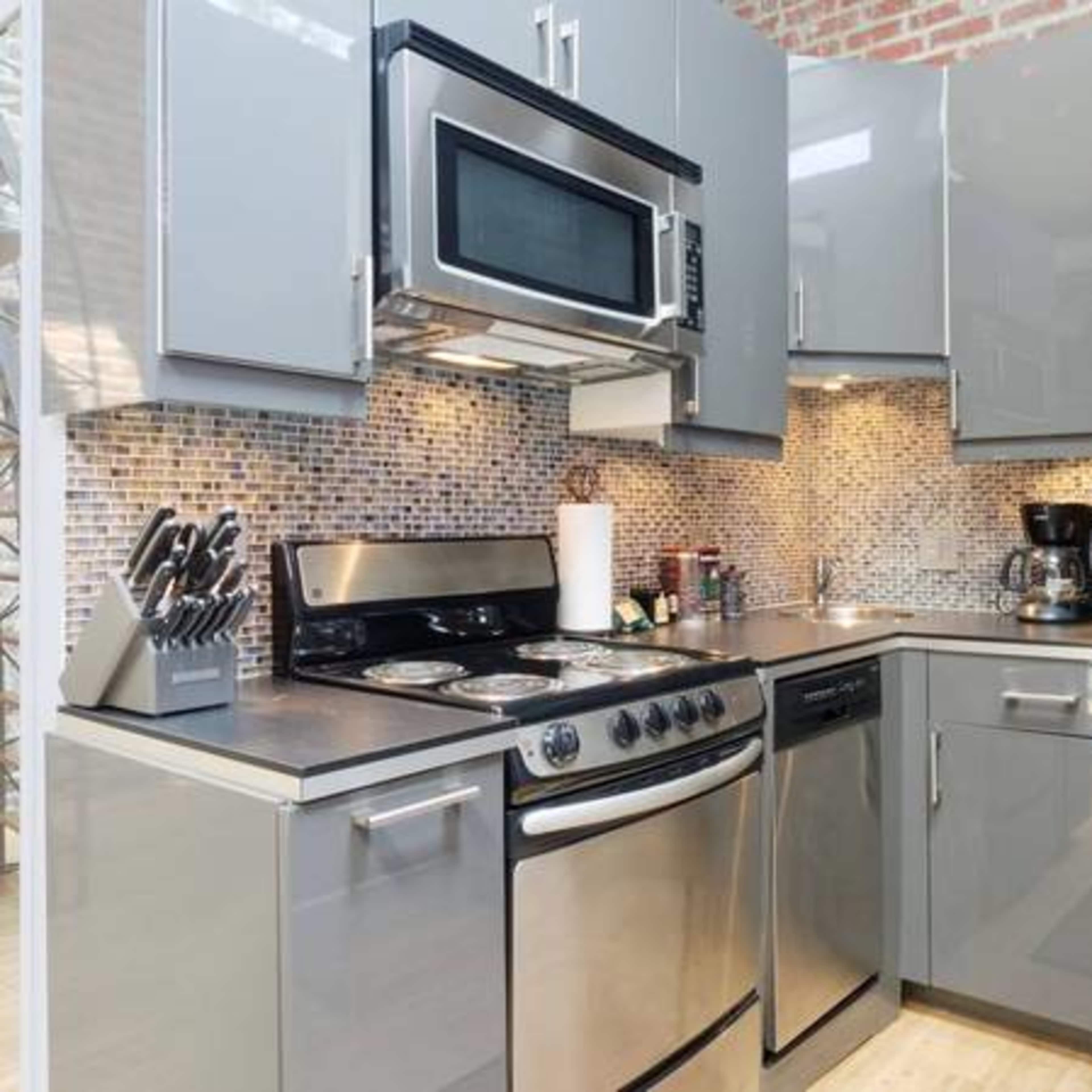 A modern kitchen with stainless steel appliances, gray cabinetry, and a mosaic tile backsplash.